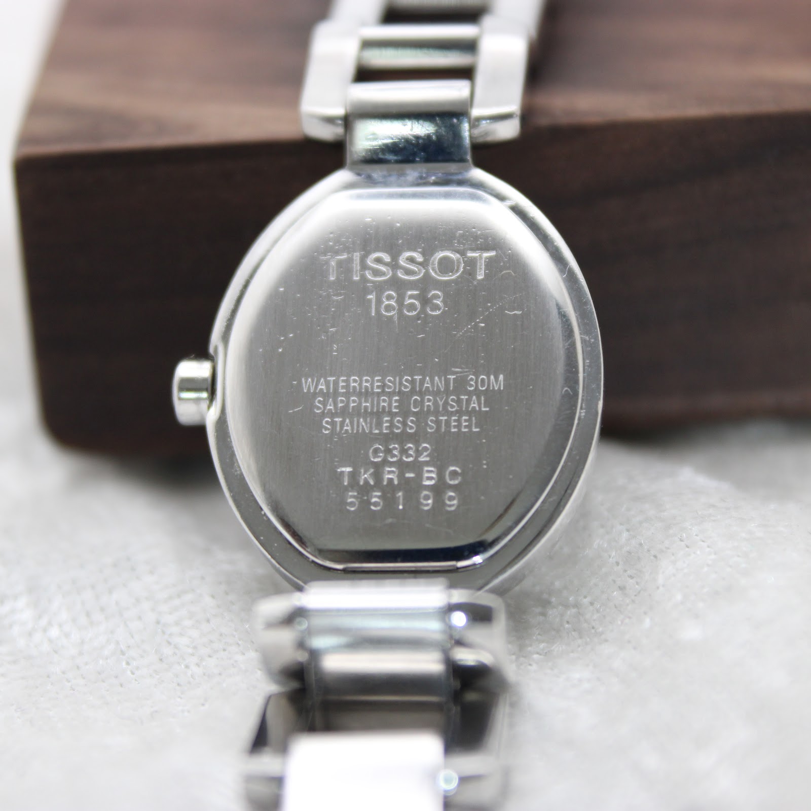 Close-up of the Tissot G332 watch case back engraving, detailing 'TISSOT 1853', 'WATER RESISTANT 30M', 'SAPPHIRE CRYSTAL', 'STAINLESS STEEL', and model 'G332 TKR-BC 55199'.