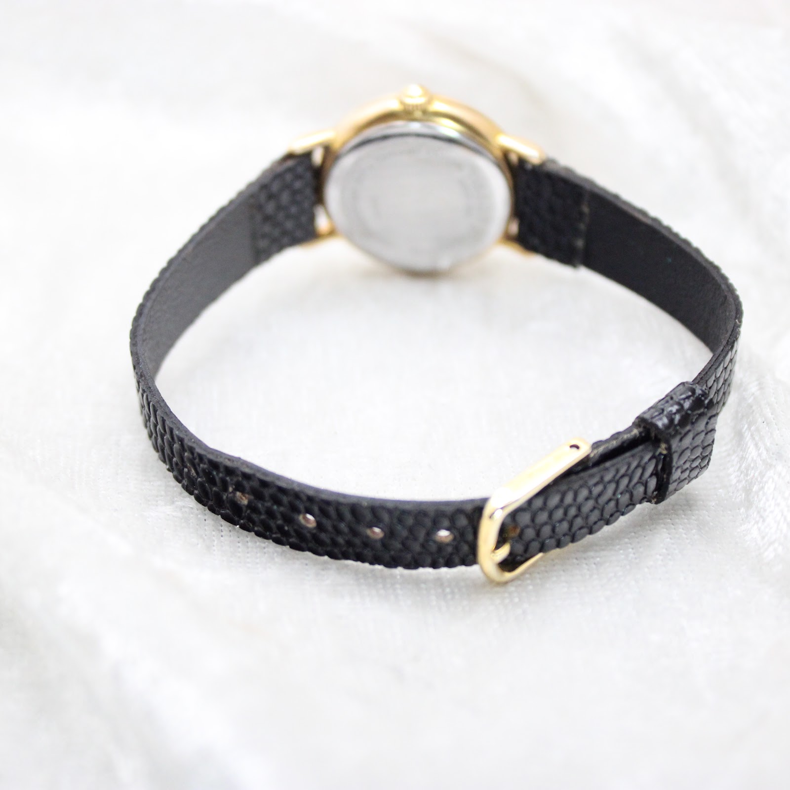 Rear view of the Tissot T852K watch, displaying the black textured leather strap with its gold-tone pin buckle against a white background.