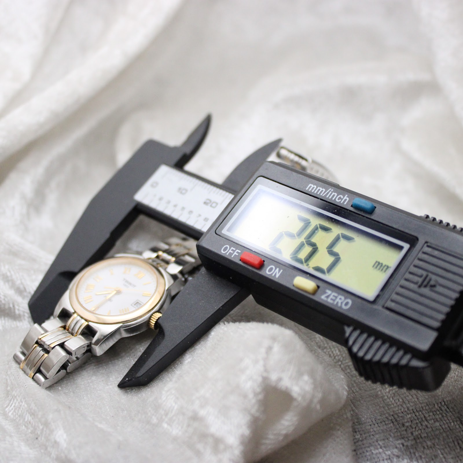 Digital caliper measuring the Tissot PR 50 watch case diameter at 26.5mm, excluding the crown.
