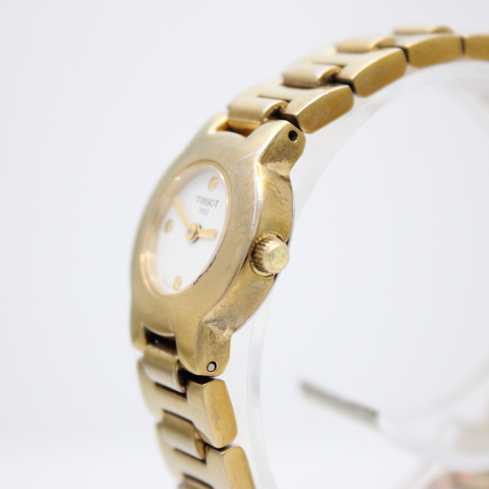 Angled view of the Tissot G331K gold watch, showing the right side of the case, crown, and integrated bracelet.