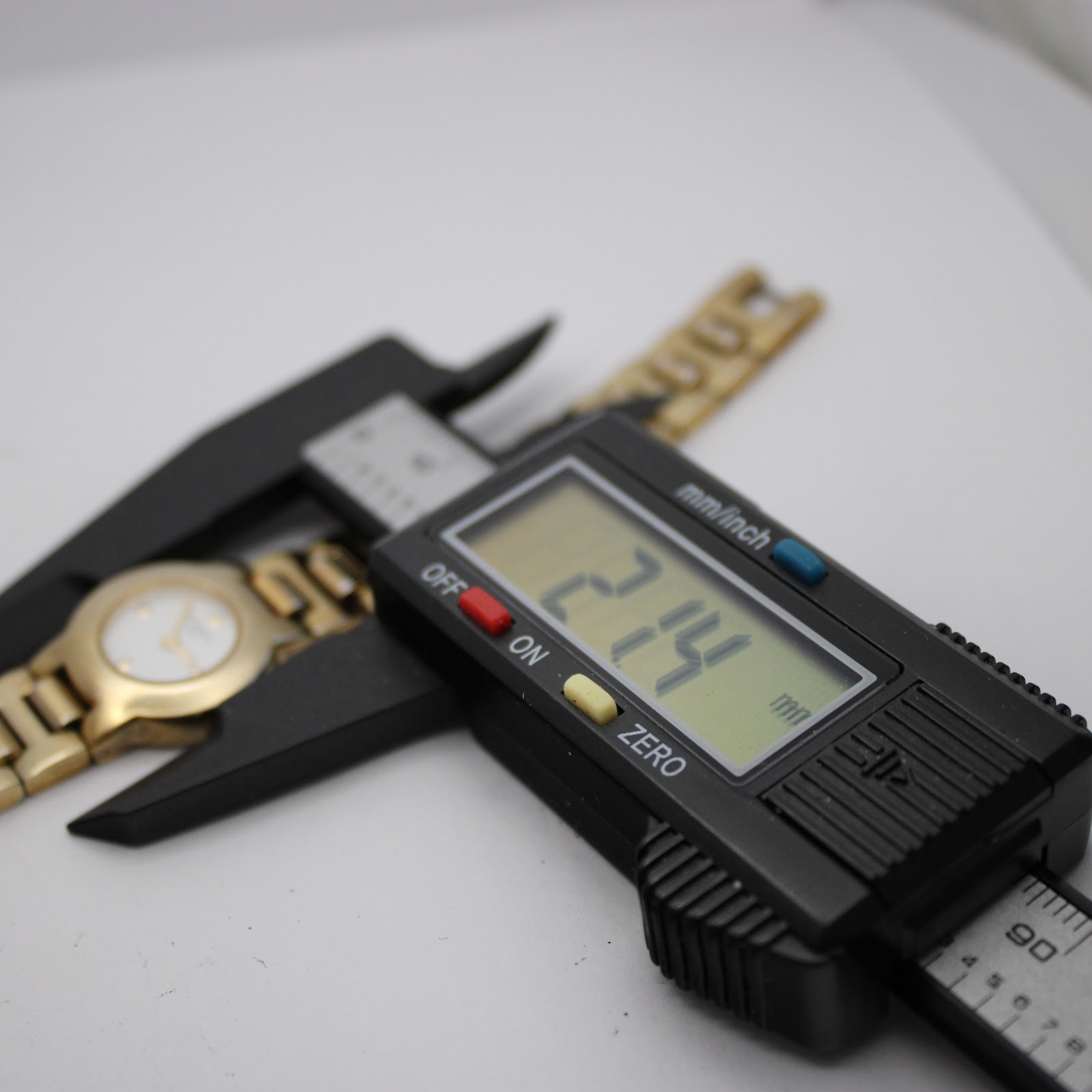 Close-up of a digital caliper measuring the case size of the Tissot watch at 21.4mm, with the watch lying on a white surface.