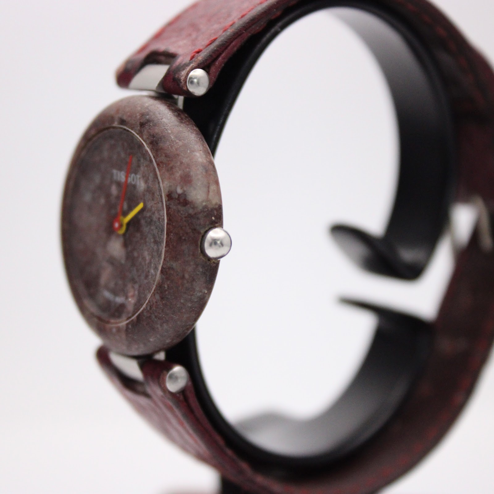 Angled side view of the Tissot Rock Watch R150, highlighting the integrated red leather strap and the natural texture of the stone case.