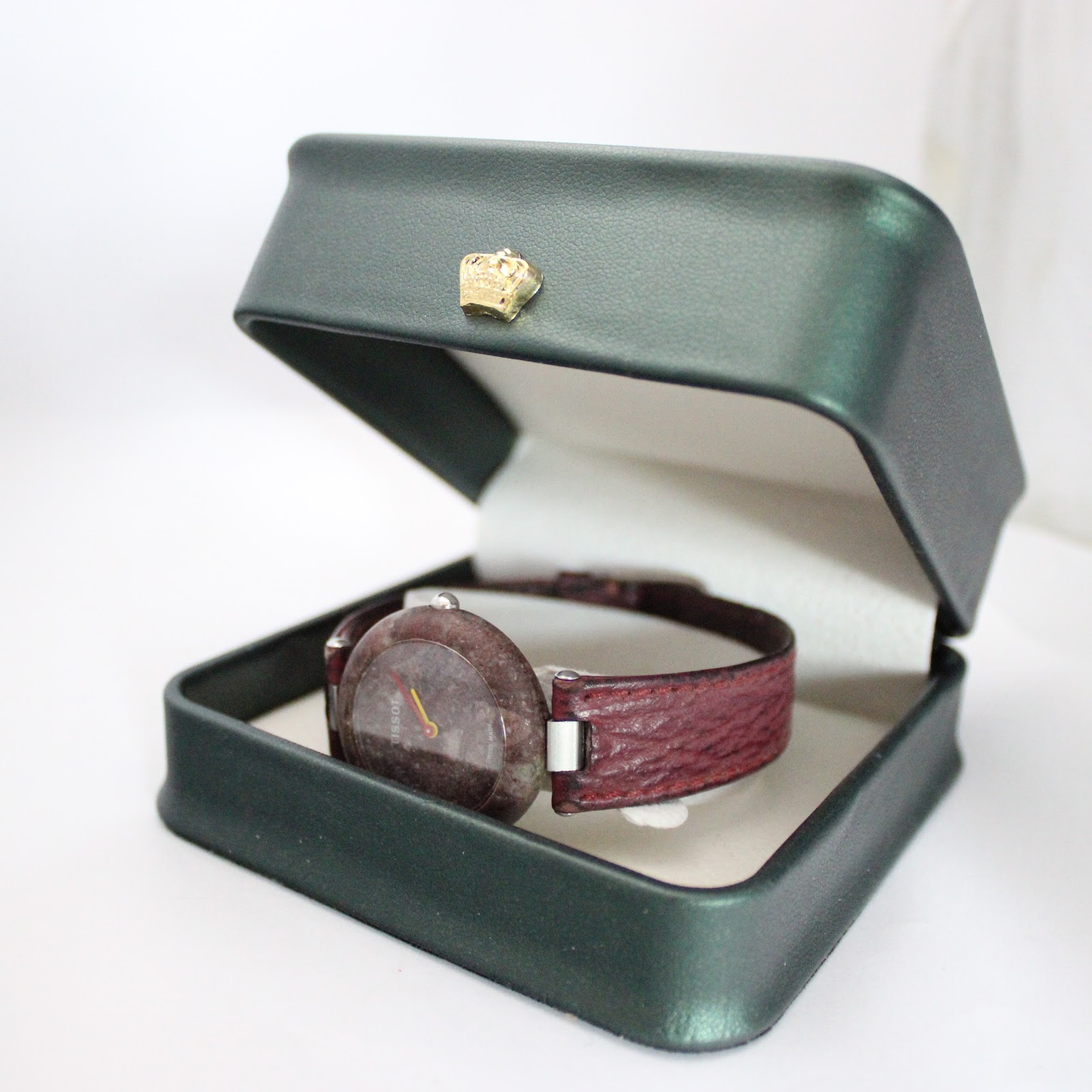 The Tissot Rock Watch R150 with its red stone case and strap, presented in an open dark green display box.