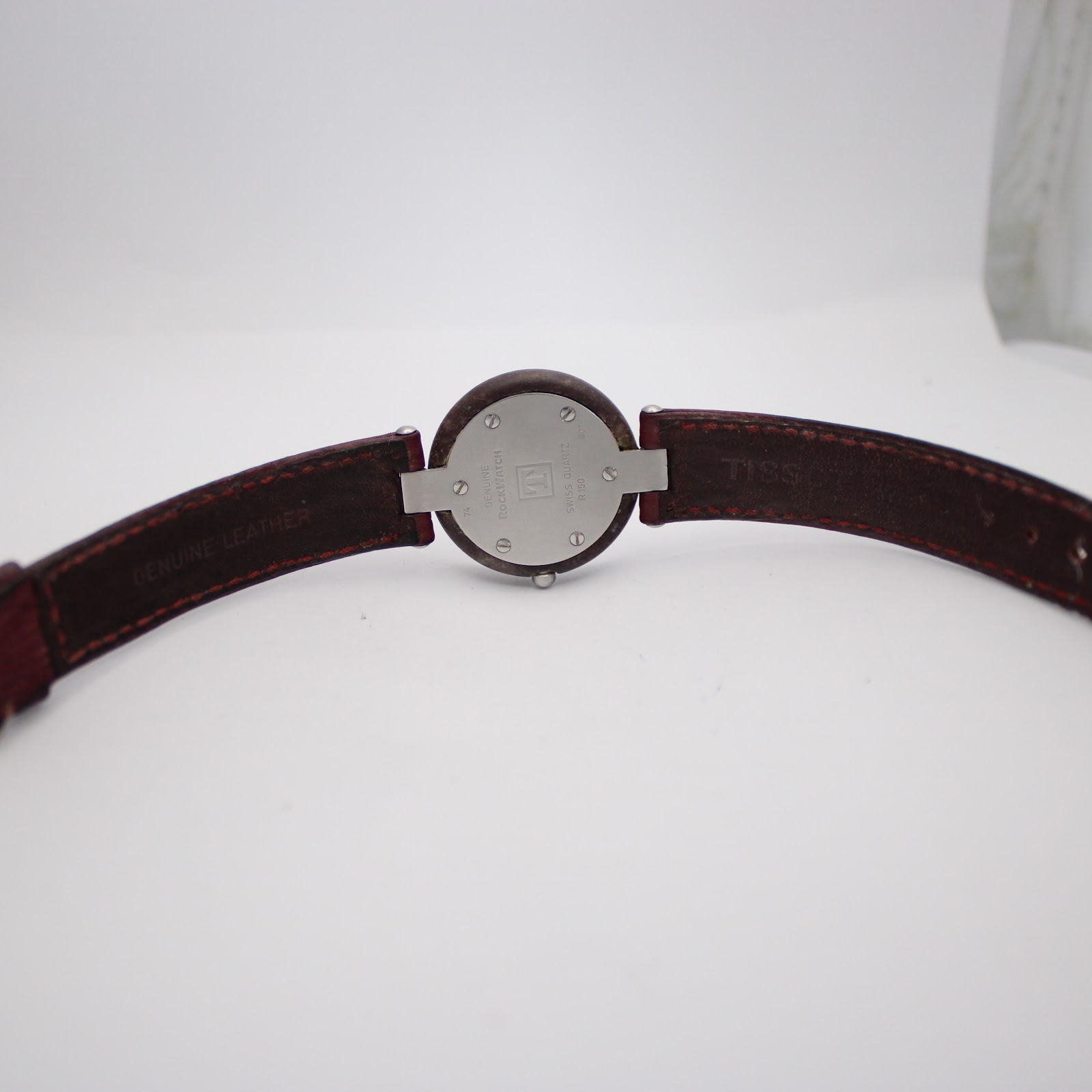 Overhead view of the Tissot Rock Watch with the red leather strap laid open, showing the "TISSOT" branding and "GENUINE LEATHER" stamp on the underside.