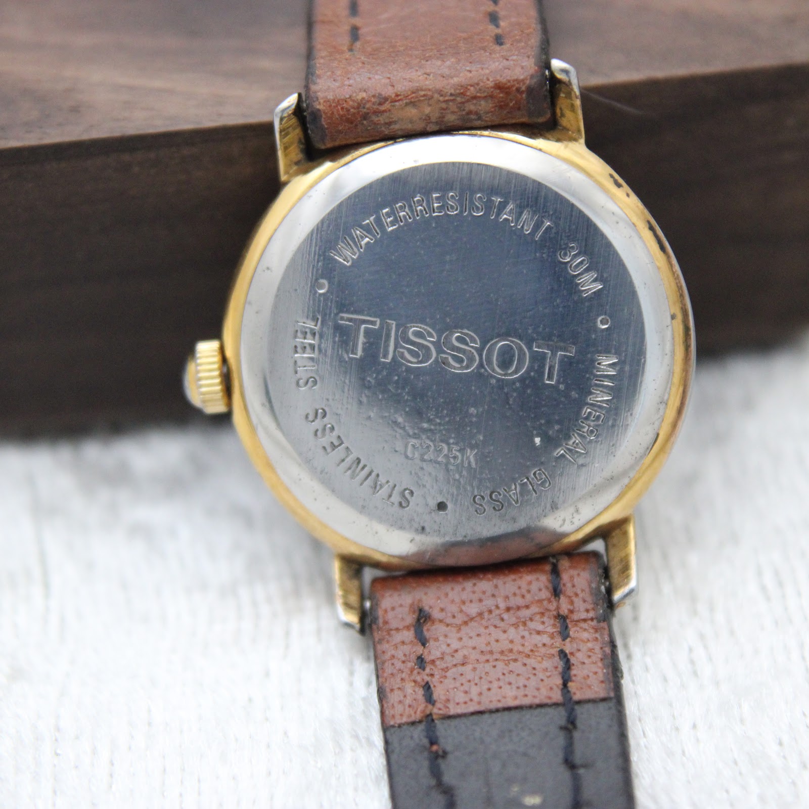 Close-up of the watch case back, showing "Waterresistant 30M", "Tissot", "Stainless Steel", "Mineral Glass", and model number C225K. The gold-tone underside of the lugs is also visible.