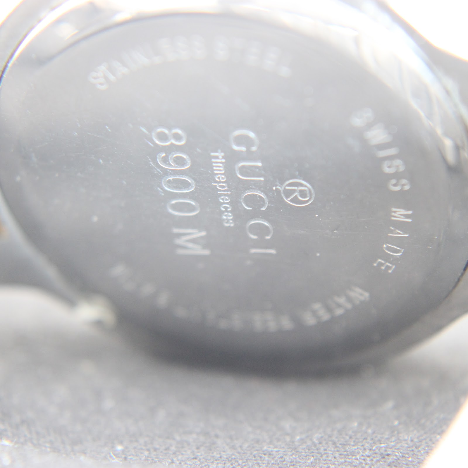 Extreme close-up of the stainless steel case back engraving, clearly showing 'GUCCI Timepieces', '8900 M', and 'SWISS MADE'.