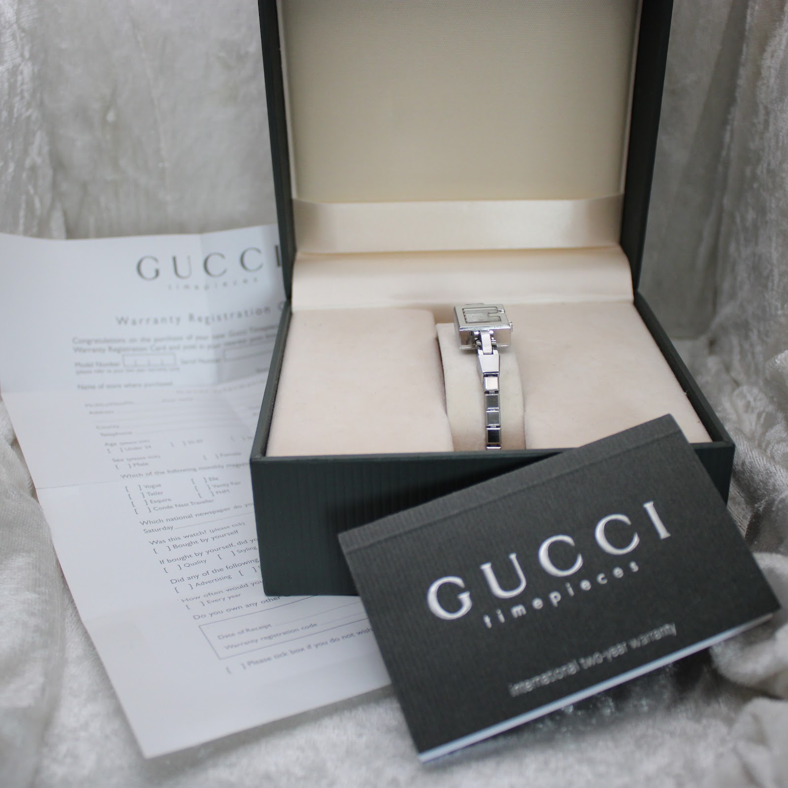 Overhead view of the Gucci 102 G-frame watch in its original box, alongside the warranty card and booklet.