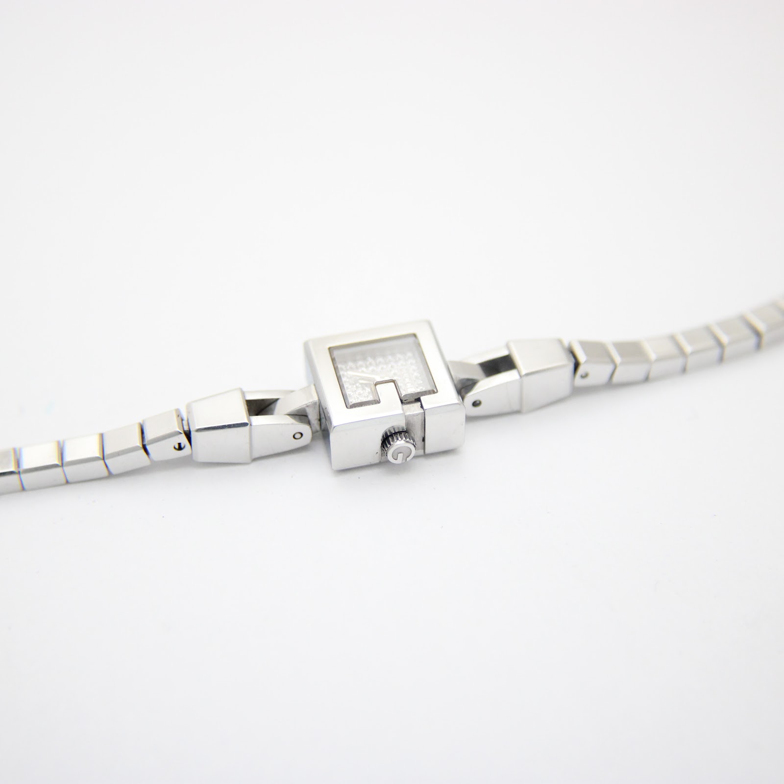 Overhead view of the Gucci 102 G-frame watch and its bracelet laid flat on a white background.