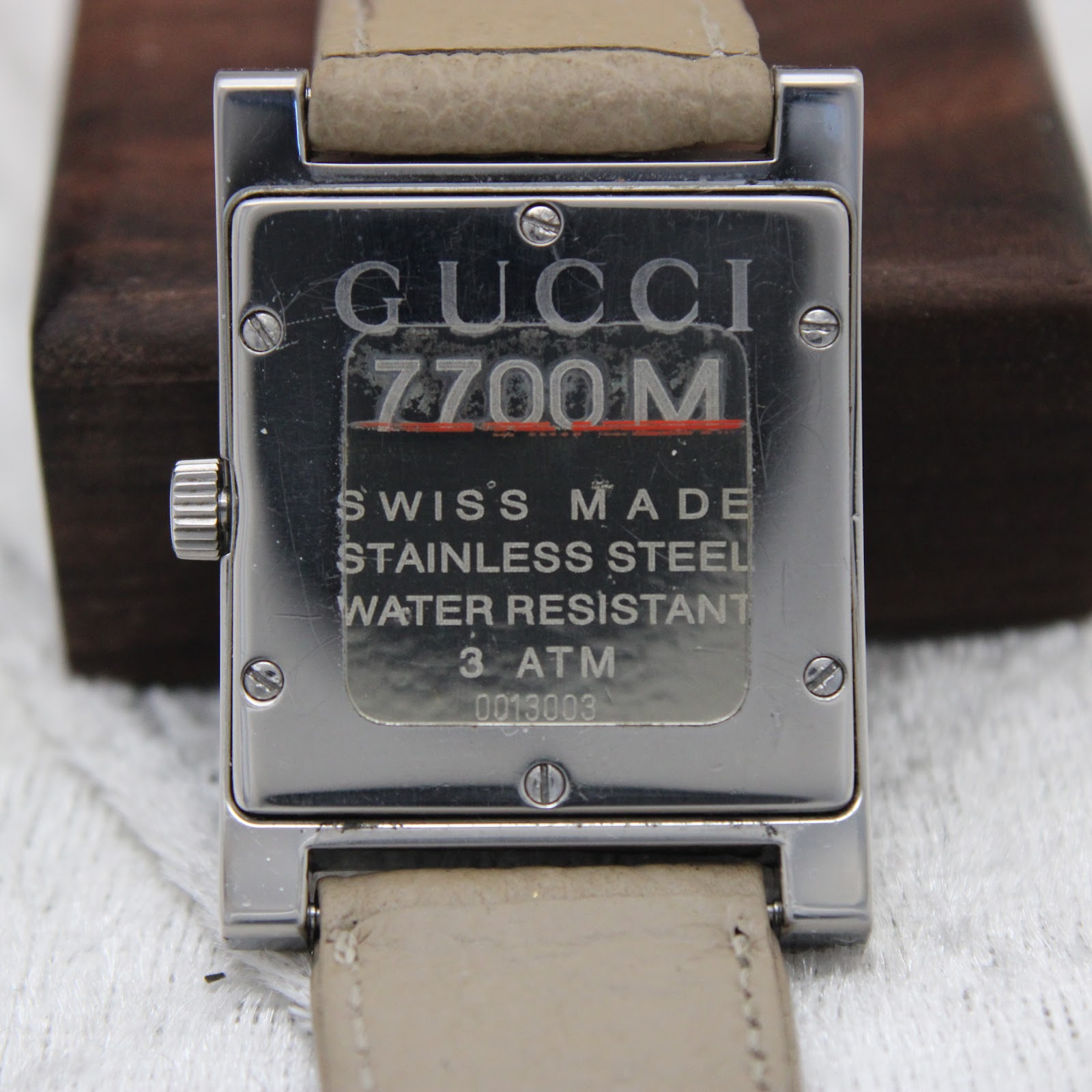 Close-up of the polished stainless steel case back with "GUCCI 7700M", "SWISS MADE", "STAINLESS STEEL", "WATER RESISTANT 3 ATM", and serial number engraving.