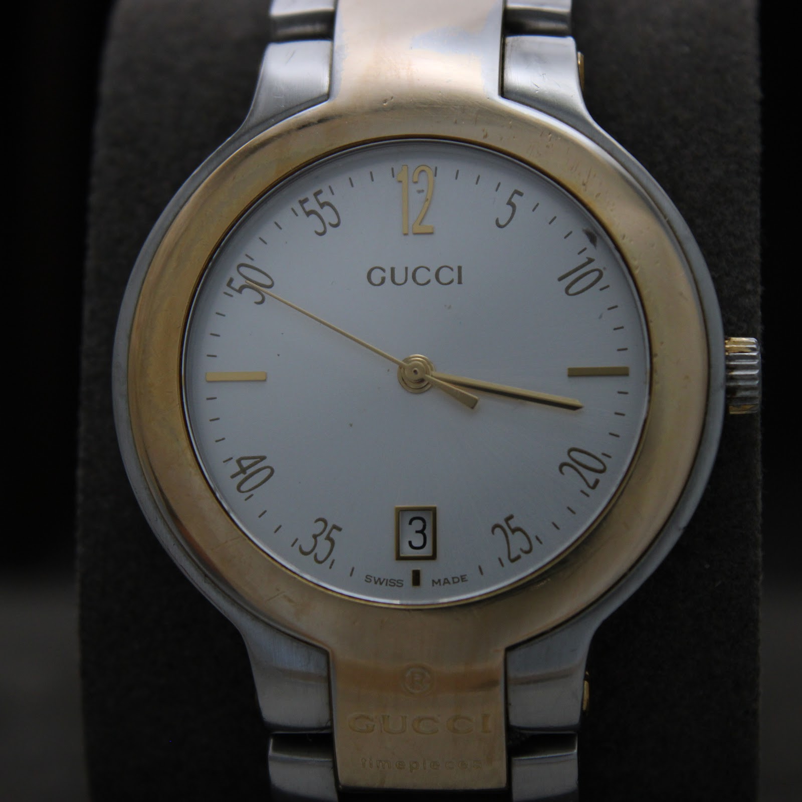 Close-up front view of the Gucci 8900M's white dial, showing gold-tone markers, hands, and a date window at 6 o'clock.