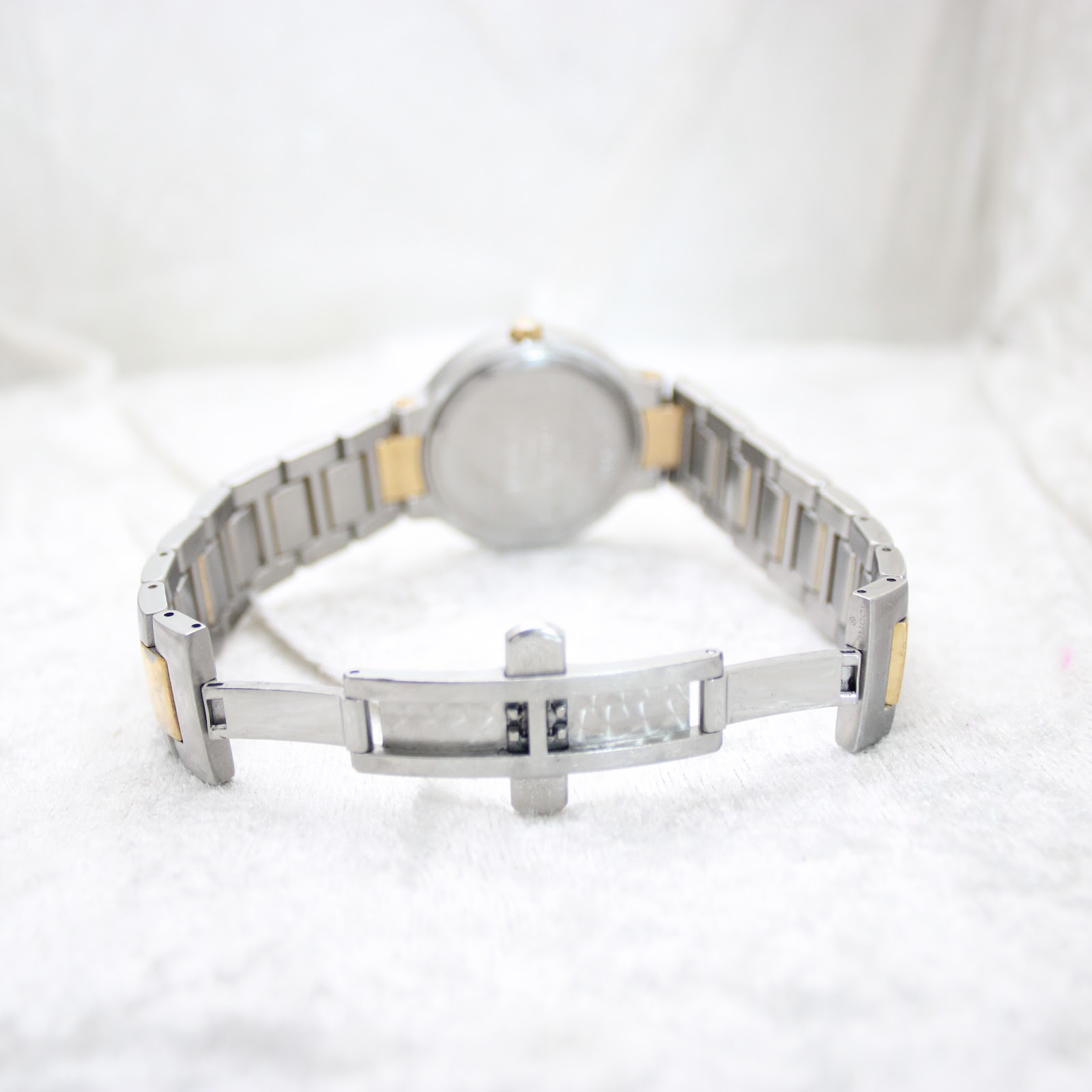 View of the watch from the back, showing the two-tone bracelet and its deployment clasp on a light-coloured surface.