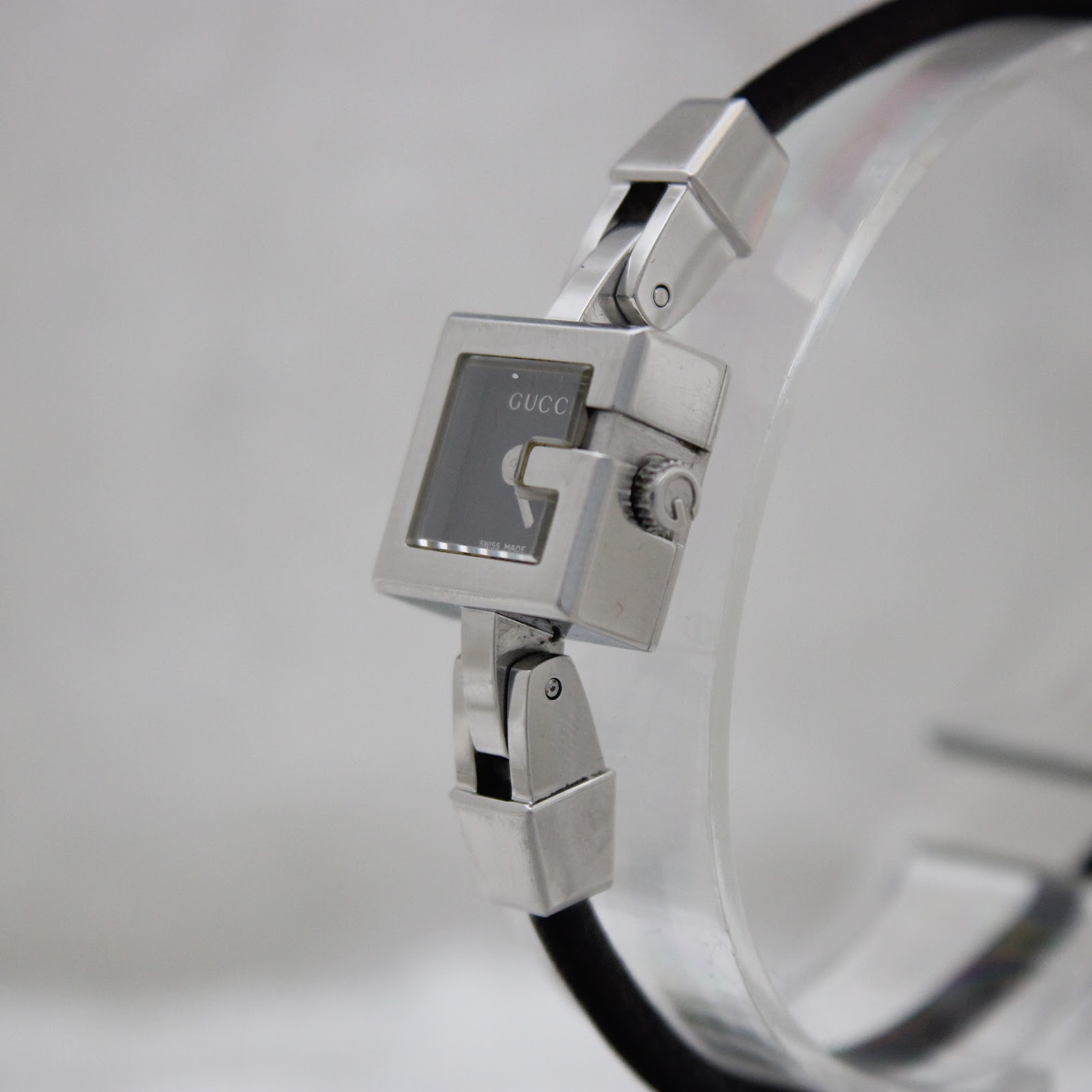 Angled close-up view of the Gucci 102 watch, highlighting the G-shaped crown detail and the polished stainless steel case.
