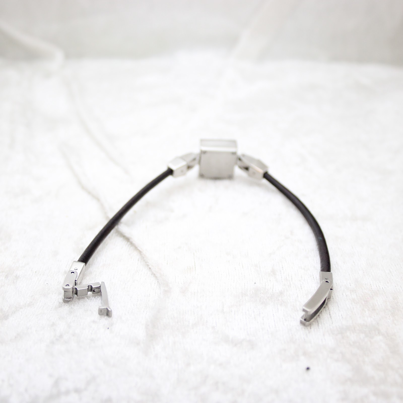Full view of the Gucci 102 watch with its black leather cord strap unclasped, laid out on a soft white surface.