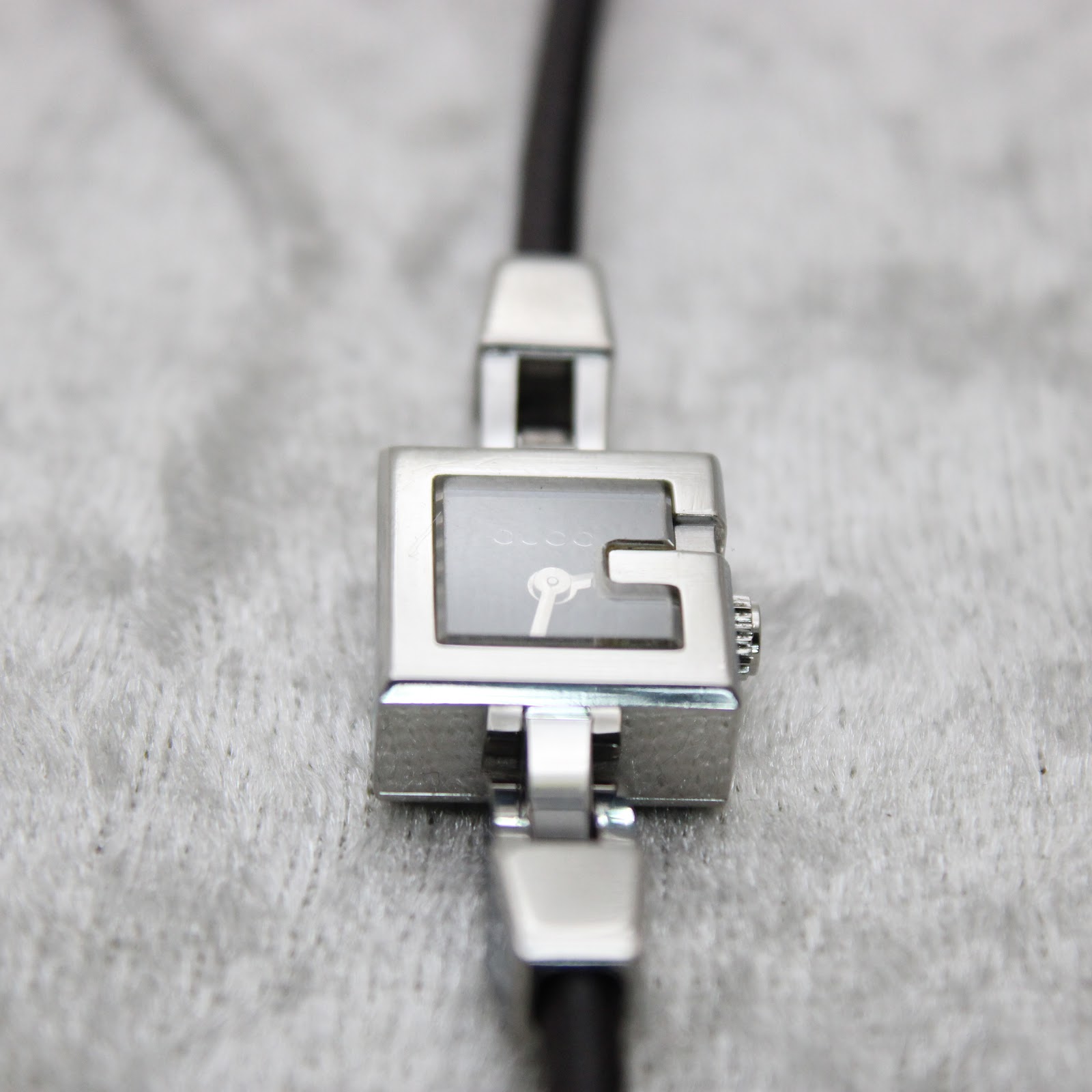 Macro close-up of the watch dial, showing the black face, silver-tone hands, 'GUCCI' logo, and 'SWISS MADE' text at 6 o'clock.