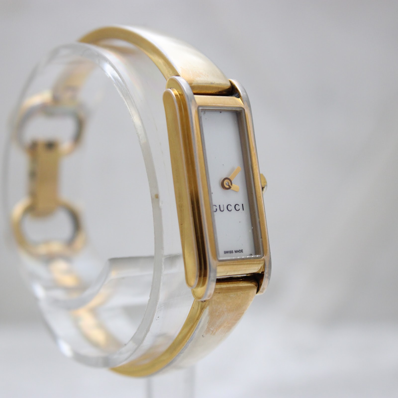 Side view of the Gucci 109 watch on a clear display stand, highlighting the rectangular case and white dial.