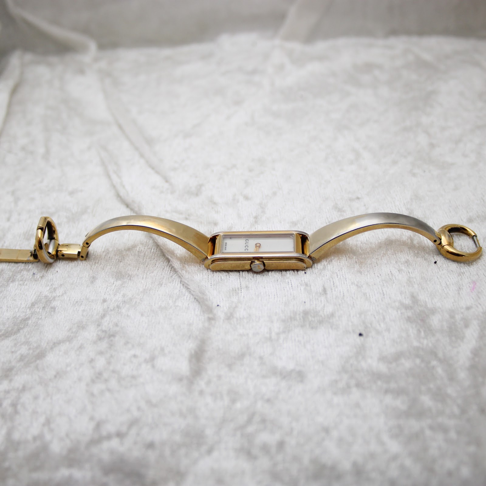 Top-down view of the opened bangle watch, revealing the full length of the gold and silver-tone bracelet.