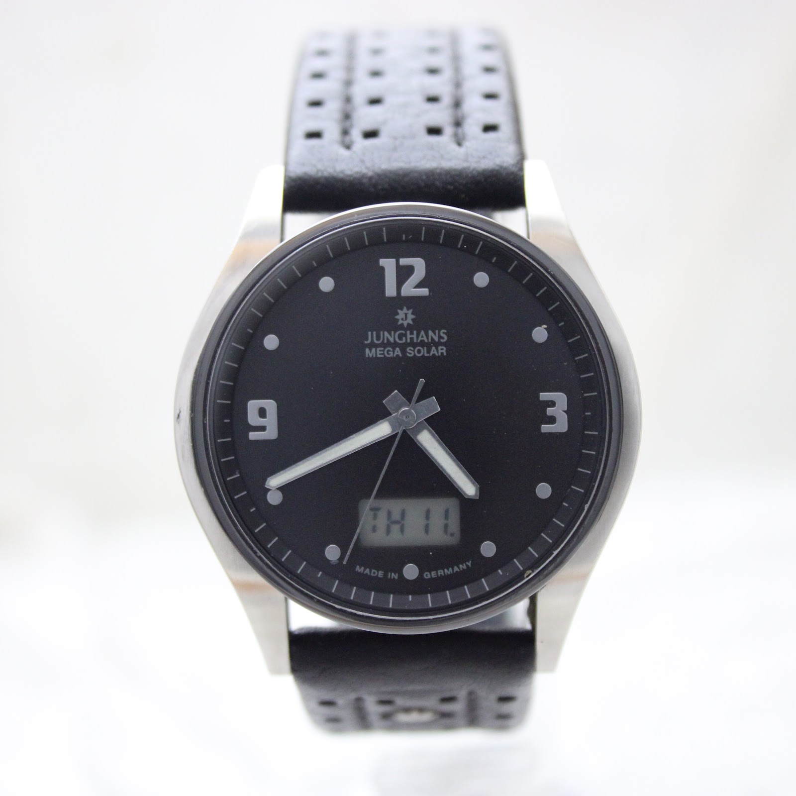Close-up front view of the Junghans Mega Solar watch dial, showing the luminous hands, numerals, and digital day/date display.