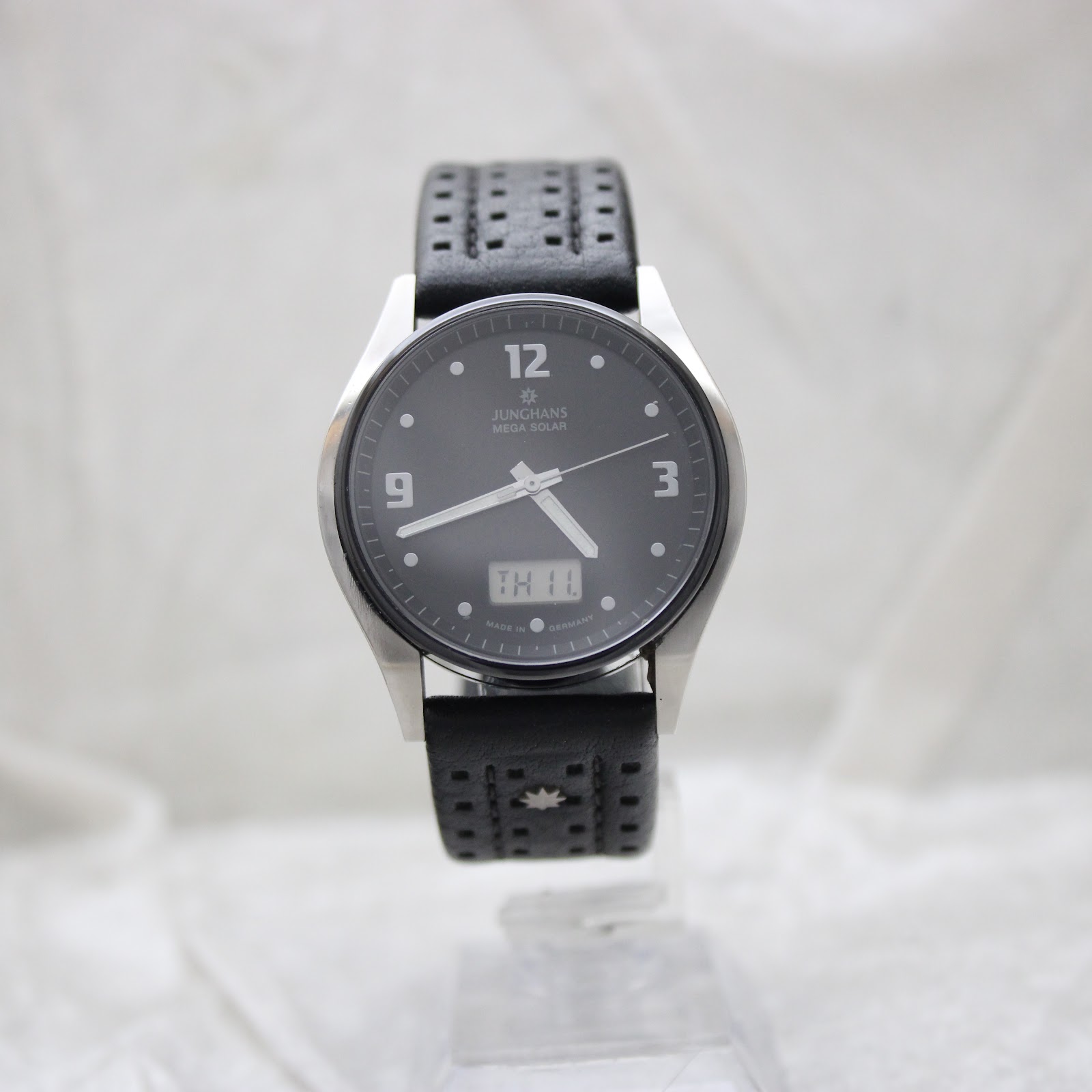 Full front view of the Junghans Mega Solar watch on a display stand, emphasising the black perforated leather strap.