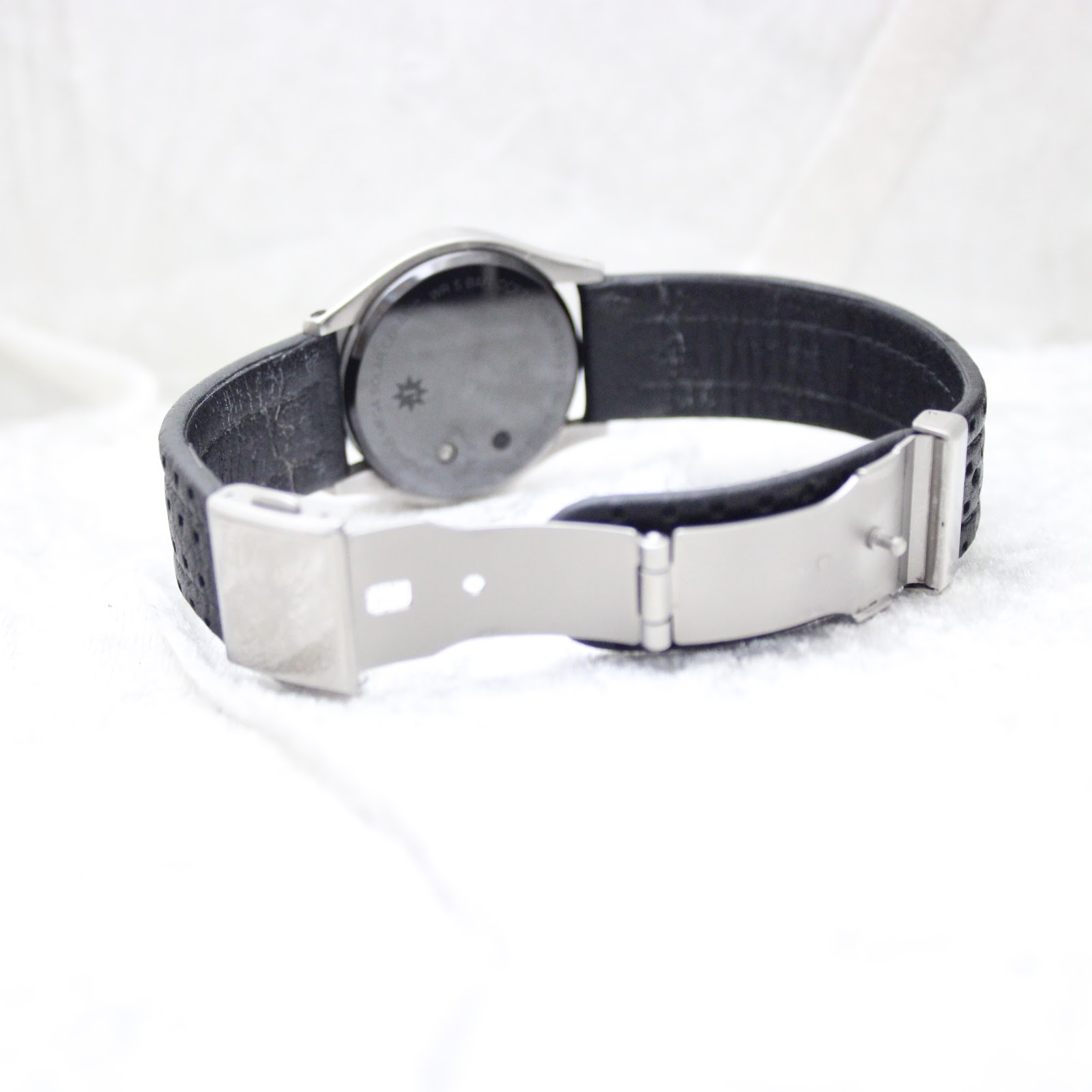 View of the watch's black perforated leather strap with its brushed stainless steel deployment clasp open.
