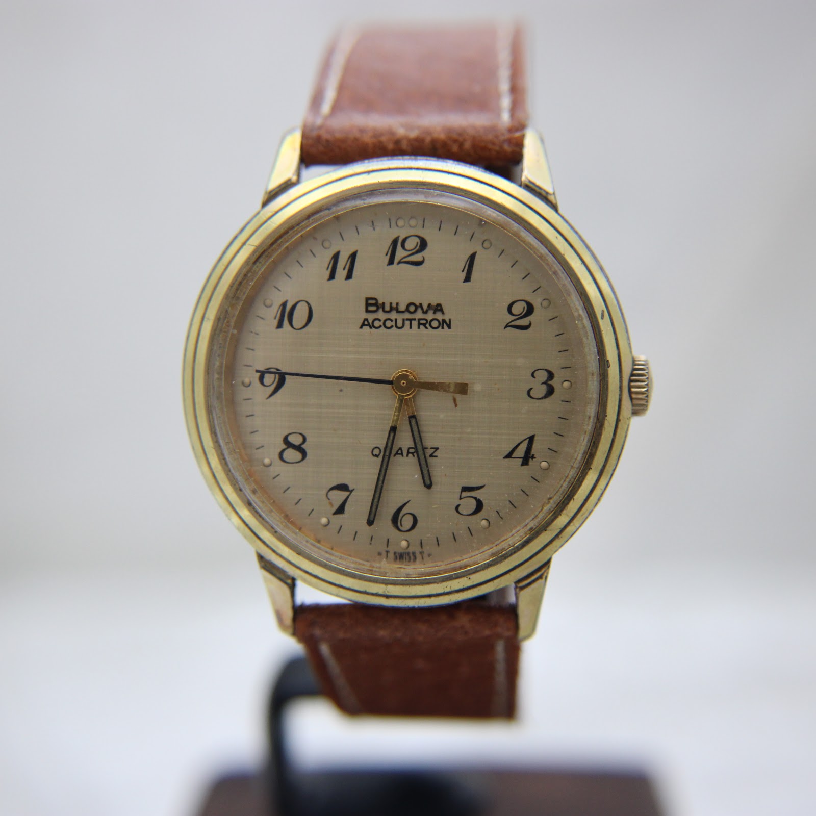 Another front view of the watch on a display stand, focusing on the champagne gold-tone dial and gold hands.