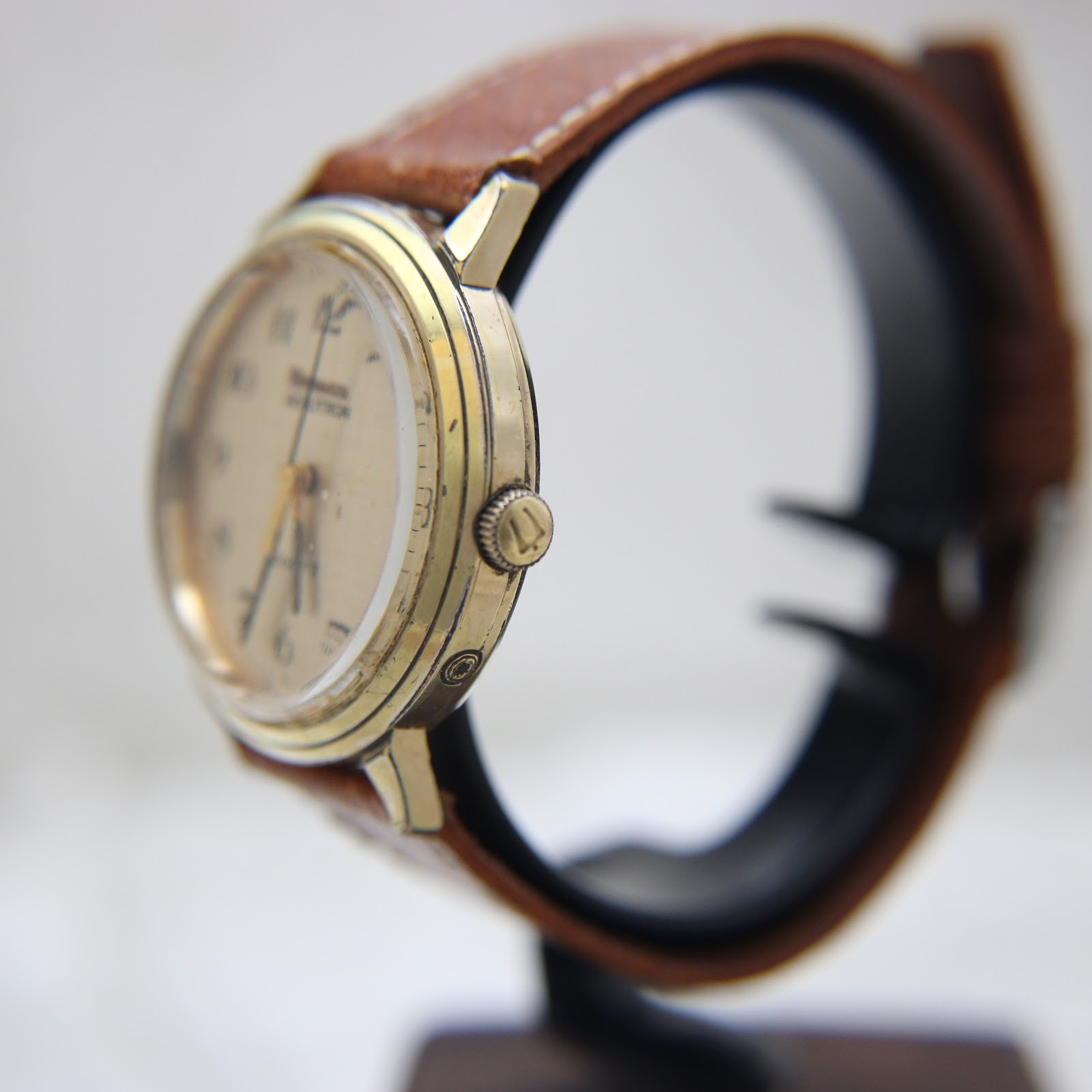 Side view of the watch on a display stand, showing the gold-plated crown and profile of the case.