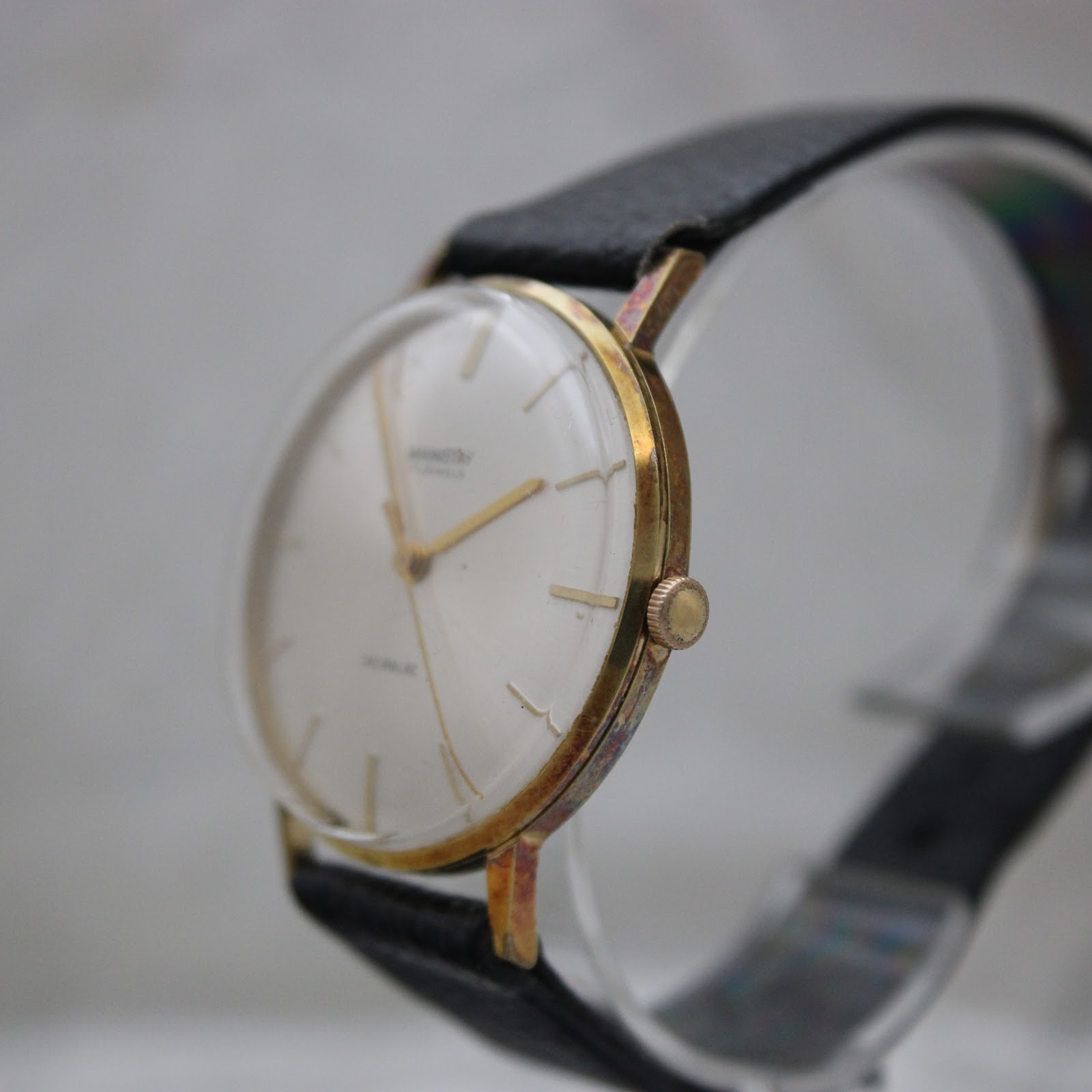 Angled side view of the Mainstay watch showing the gold-plated case and the domed acrylic crystal.