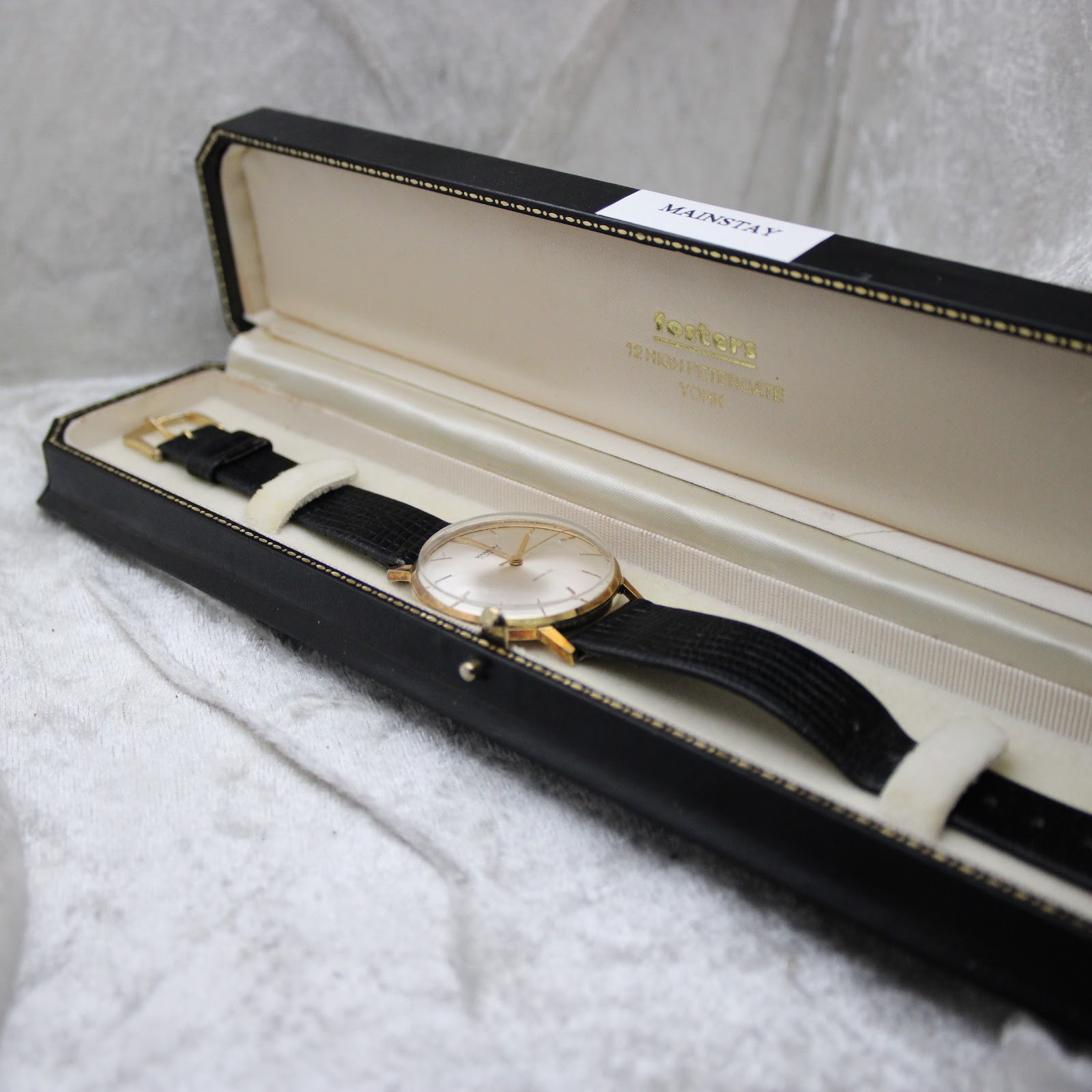 The Mainstay watch displayed in an open vintage black watch box with cream interior.