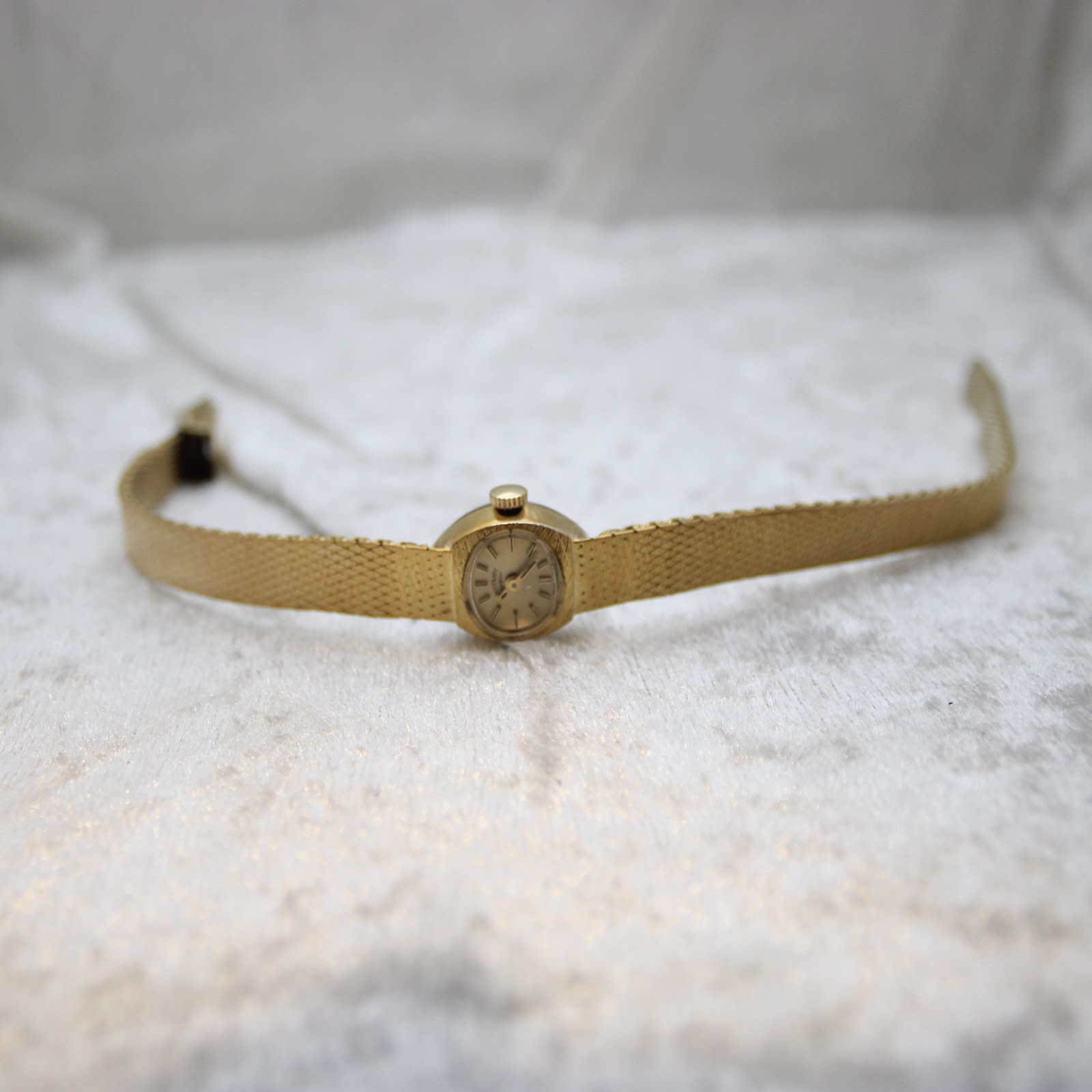 Full length view of the Rotary gold-tone watch with integrated bracelet laid out on a white textured surface.