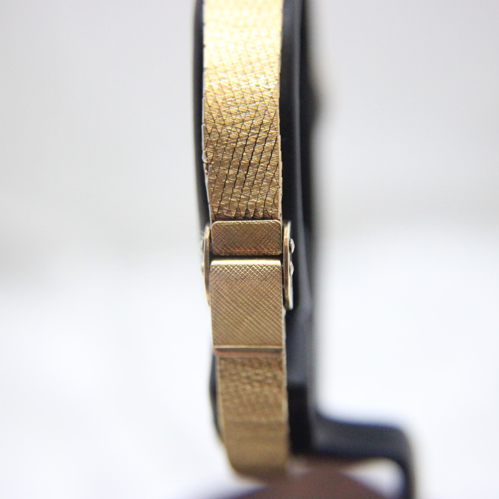 Close-up side view of the integrated gold-tone bracelet's clasp mechanism.