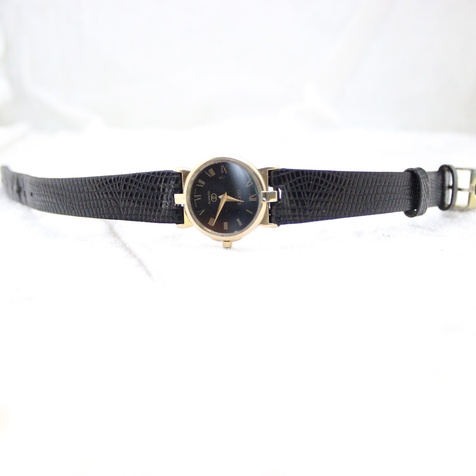 Overhead view of the entire Gucci watch, displaying the black textured leather strap and gold-plated case.