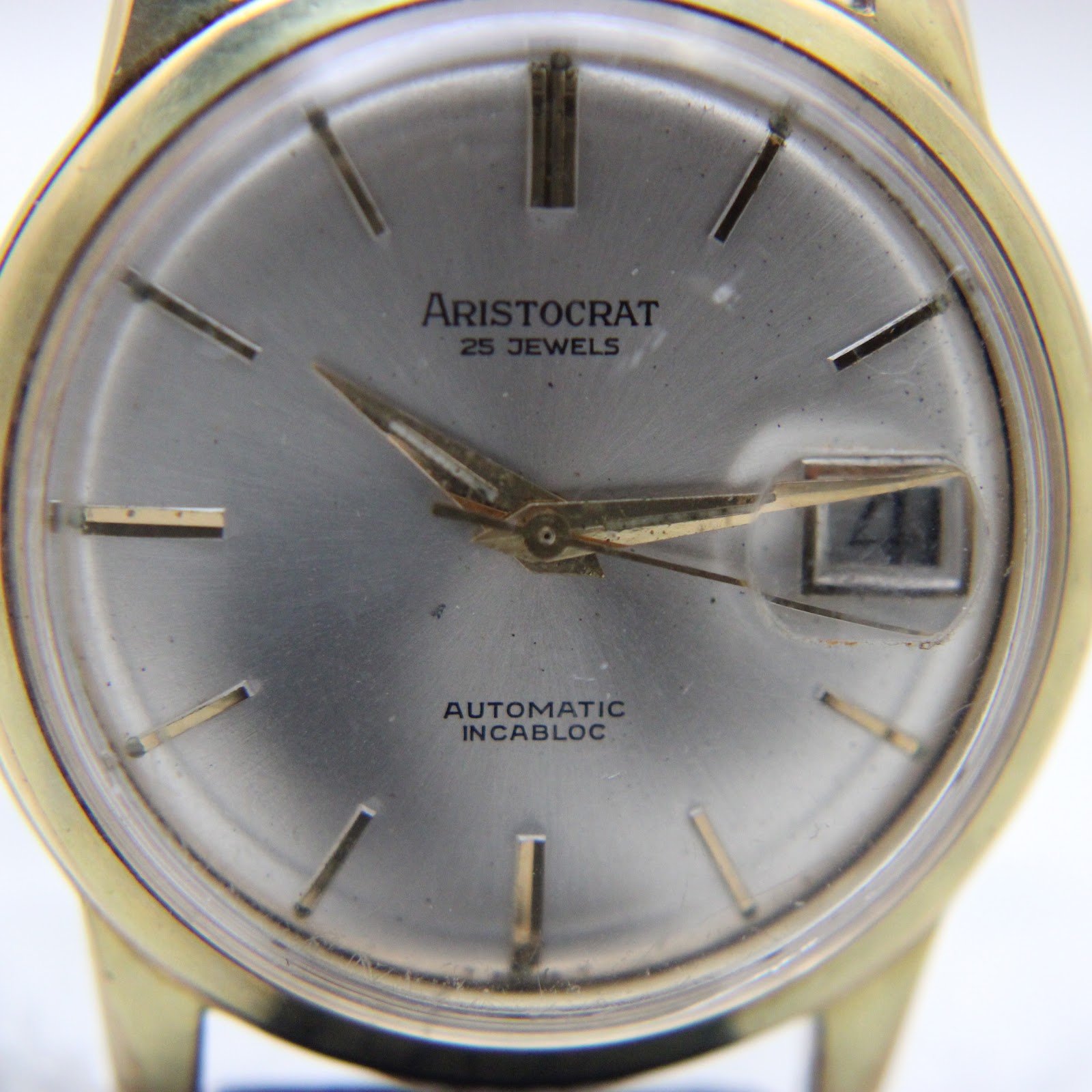 Close-up of the Aristocrat watch dial, showing the '25 jewels' text, gold-tone applied indices, and date window.