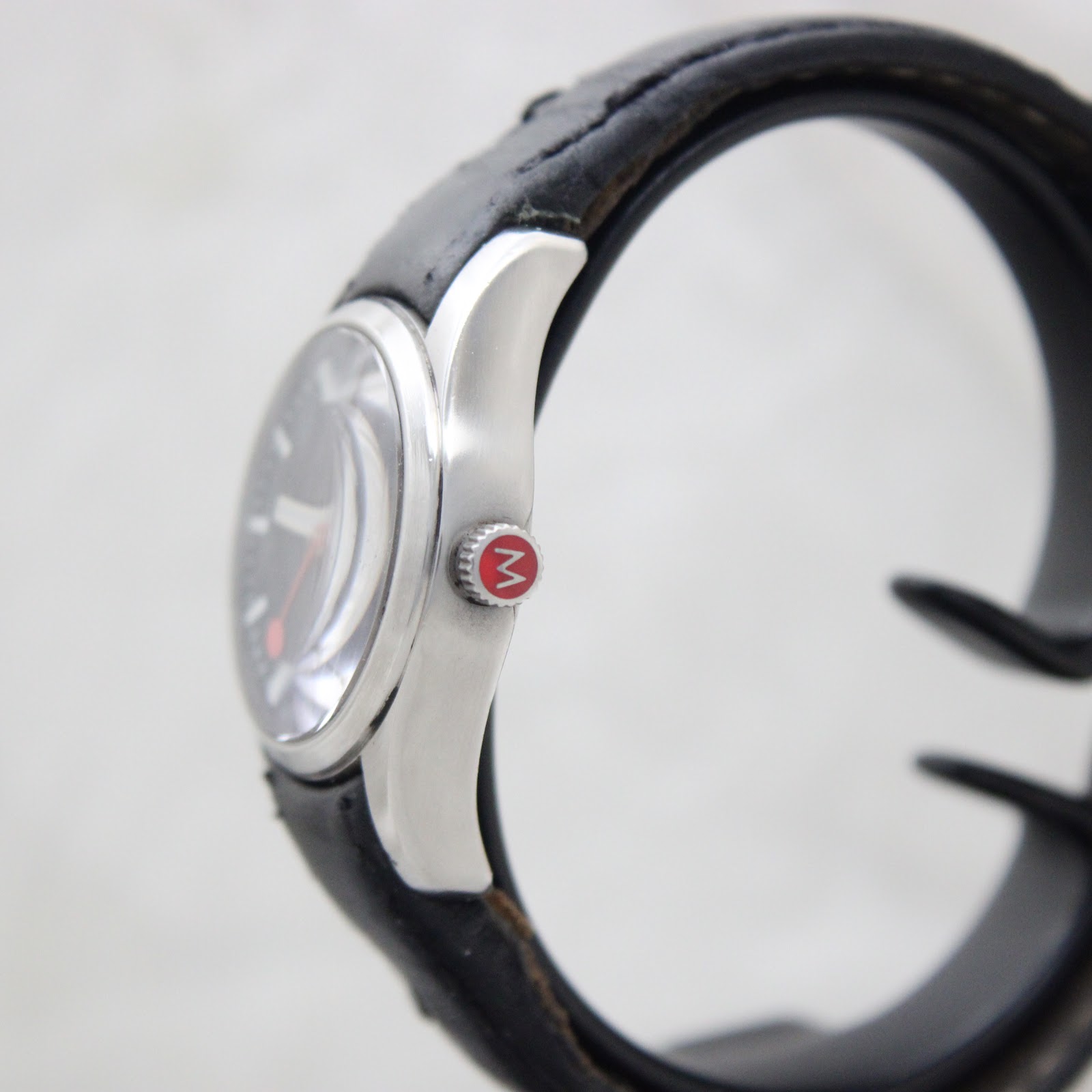 Side view of the Mondaine watch showing the brushed stainless steel case and signed crown with red 'M' logo
