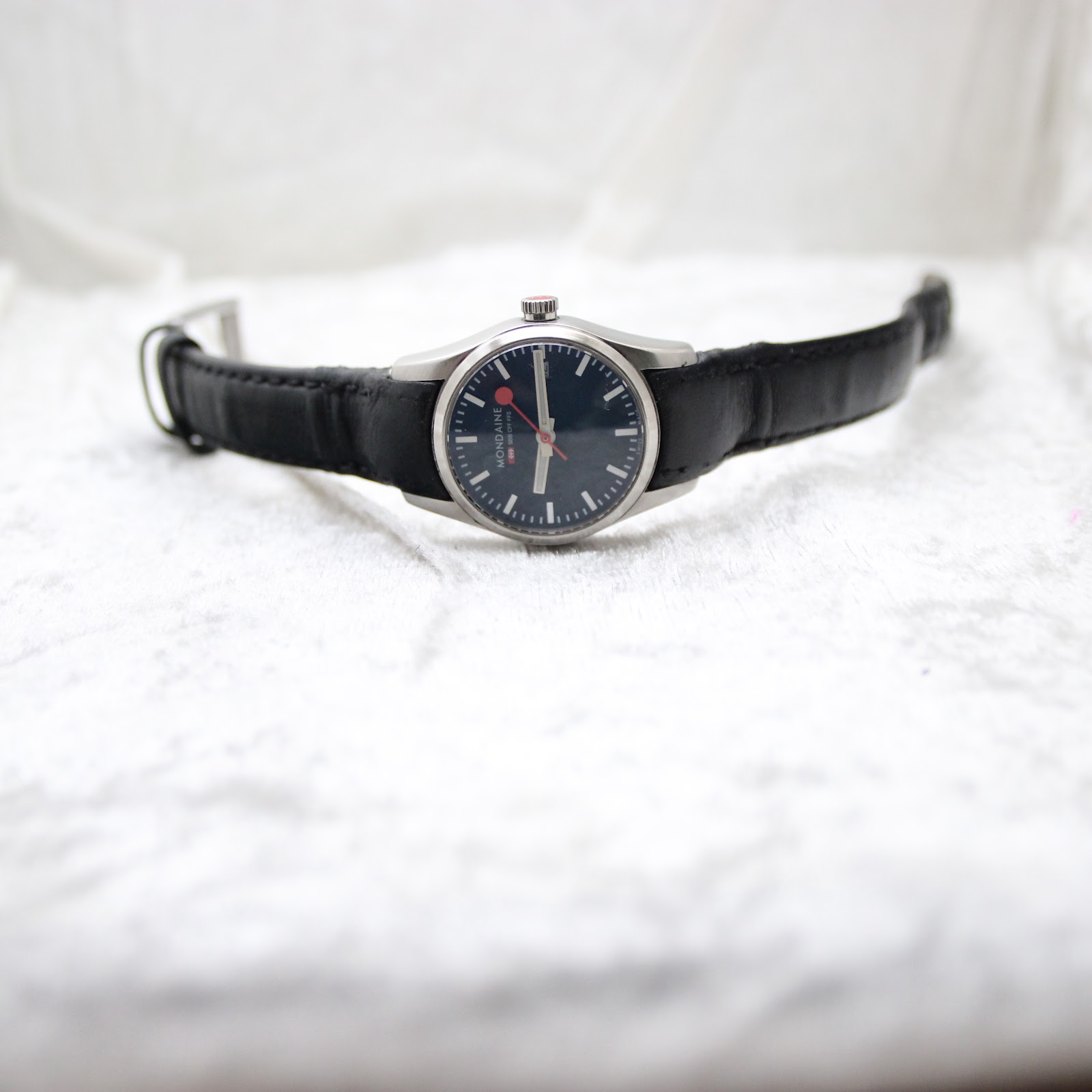 Front view of the Mondaine watch with the strap laid flat on a white textured surface