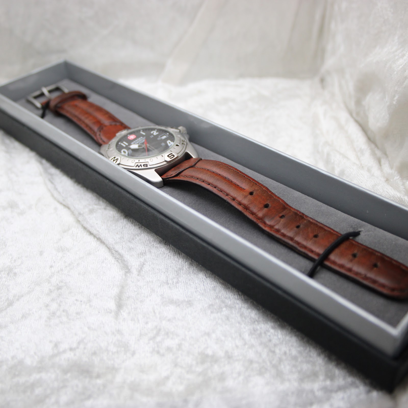 The watch presented inside a black display box, highlighting its full length and brown leather strap.