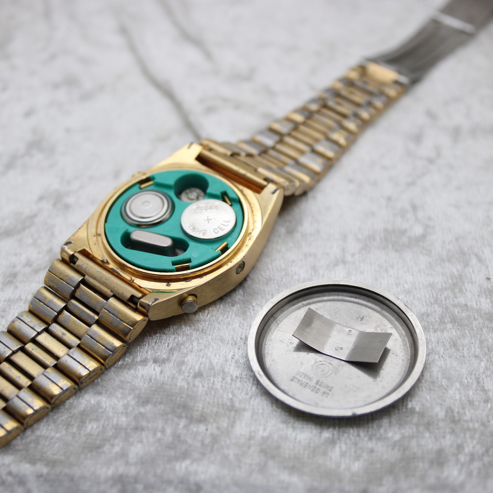 Back view of the La Générale watch with the stainless steel case back removed, revealing two batteries and the green electronic movement housing.