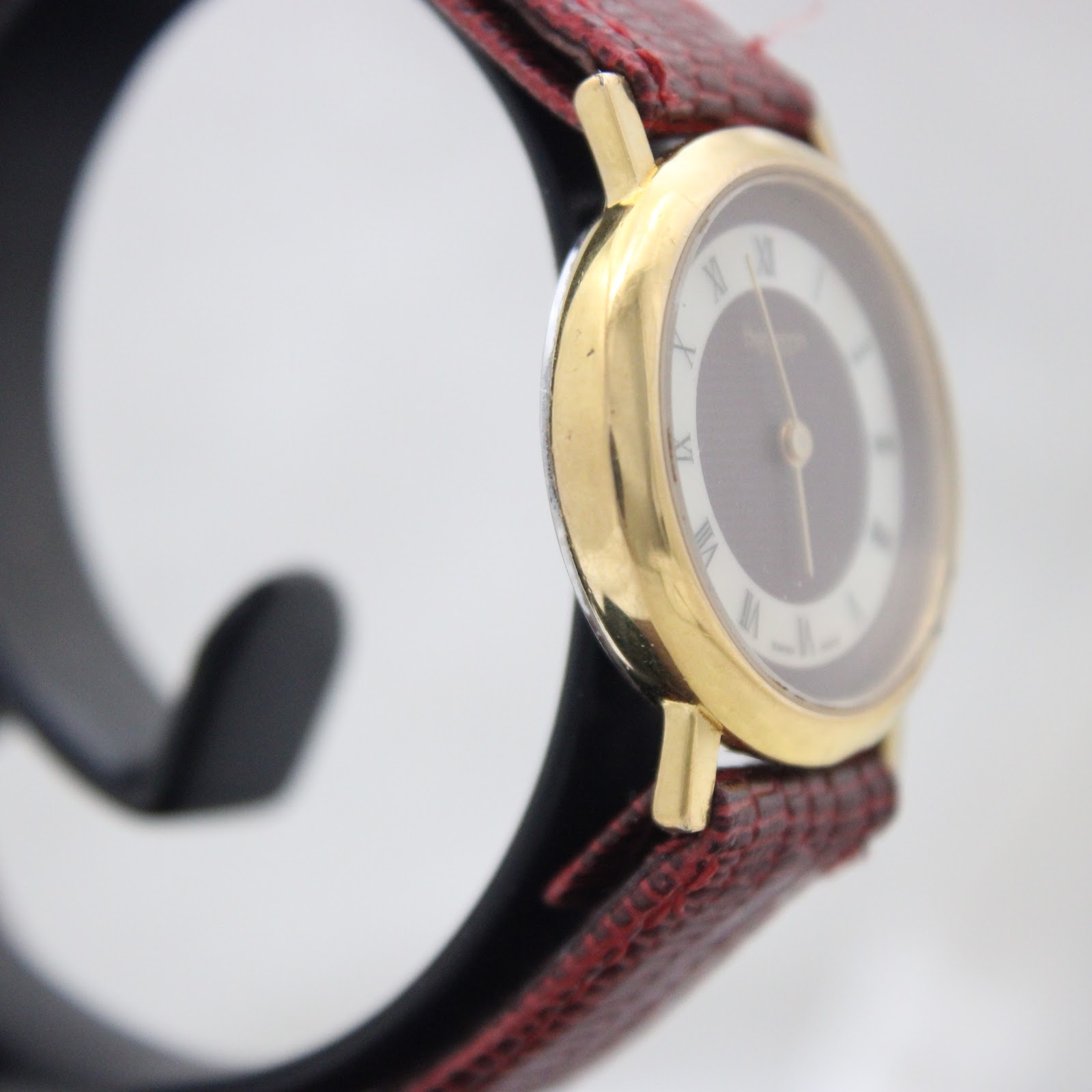 Angled side view of the gold-tone Burberrys watch case and burgundy leather strap.