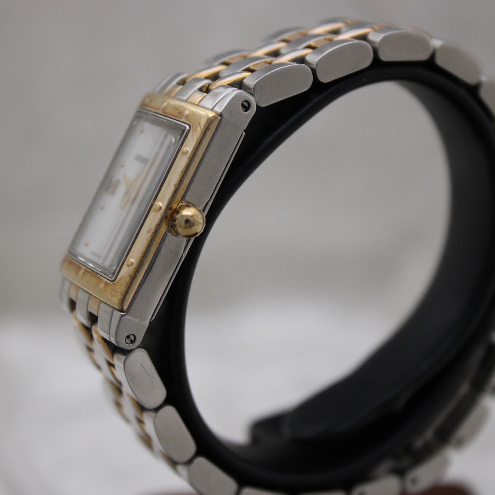Right side profile view of the Raymond Weil Tango watch on a display stand, showing the gold-tone fluted crown and case side.