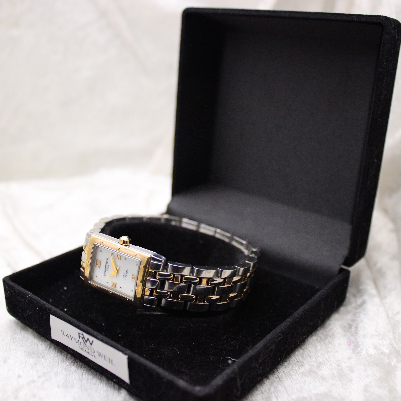 Overhead view of the Raymond Weil Tango watch resting inside a black velvet Raymond Weil presentation pouch.