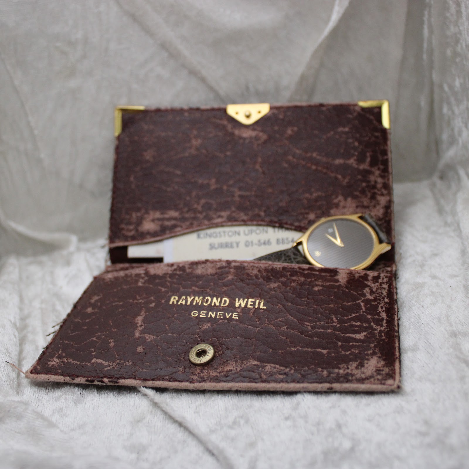 The Raymond Weil branded wallet opened, revealing the original documentation and partially showing the watch face tucked inside.