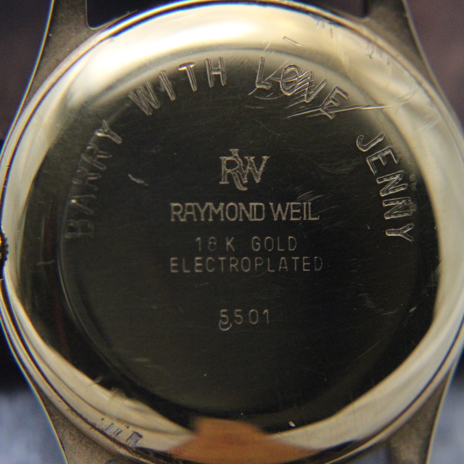 Close-up of the watch case back showing an engraved personal message 'Barry with love Jenny' and 'Raymond Weil 18K Gold Electroplated 5501'.