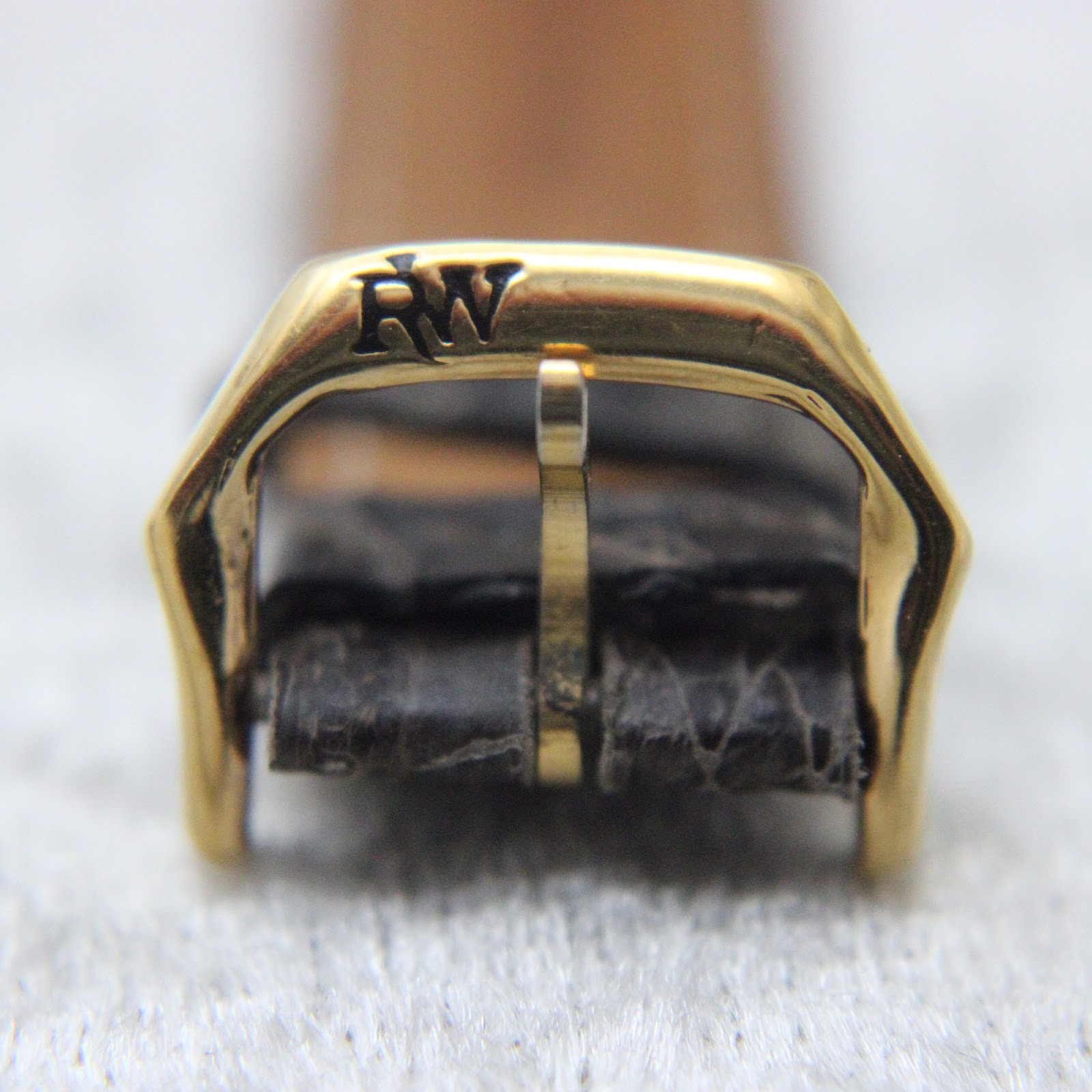 Macro shot of the gold-tone buckle, clearly displaying the iconic 'RW' Raymond Weil logo.