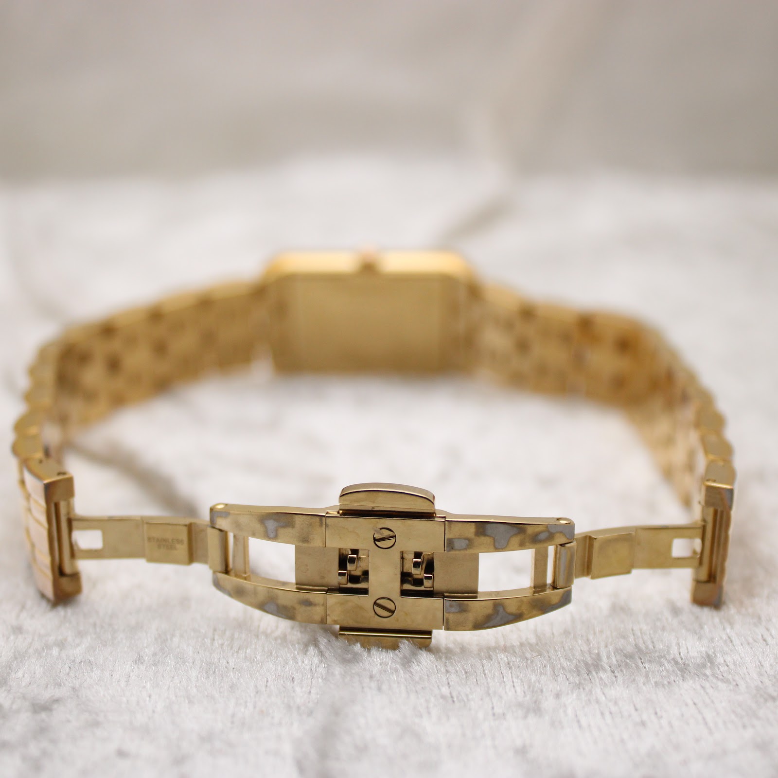 Close-up of the opened gold deployant clasp of the watch bracelet, showing 'stainless steel' inscription
