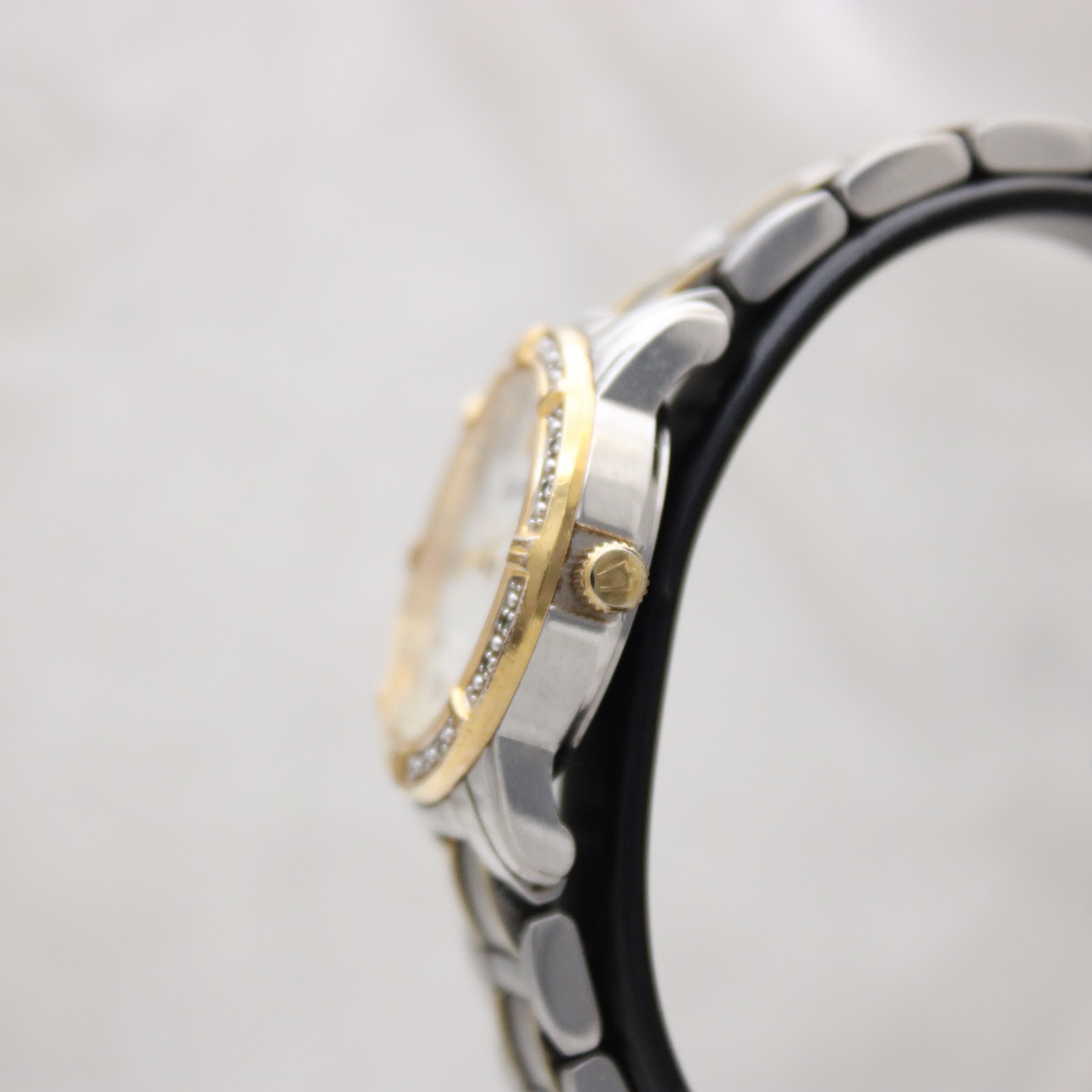 Side view of the Bulova watch case and gold-tone crown on a watch stand.