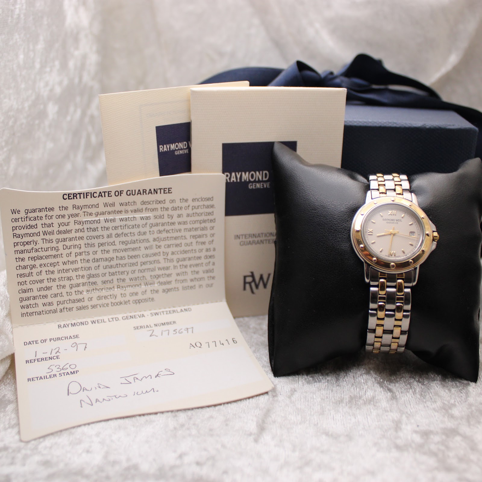 Raymond Weil watch displayed on a cushion, surrounded by its original certificate of guarantee, instruction booklet, and outer box.