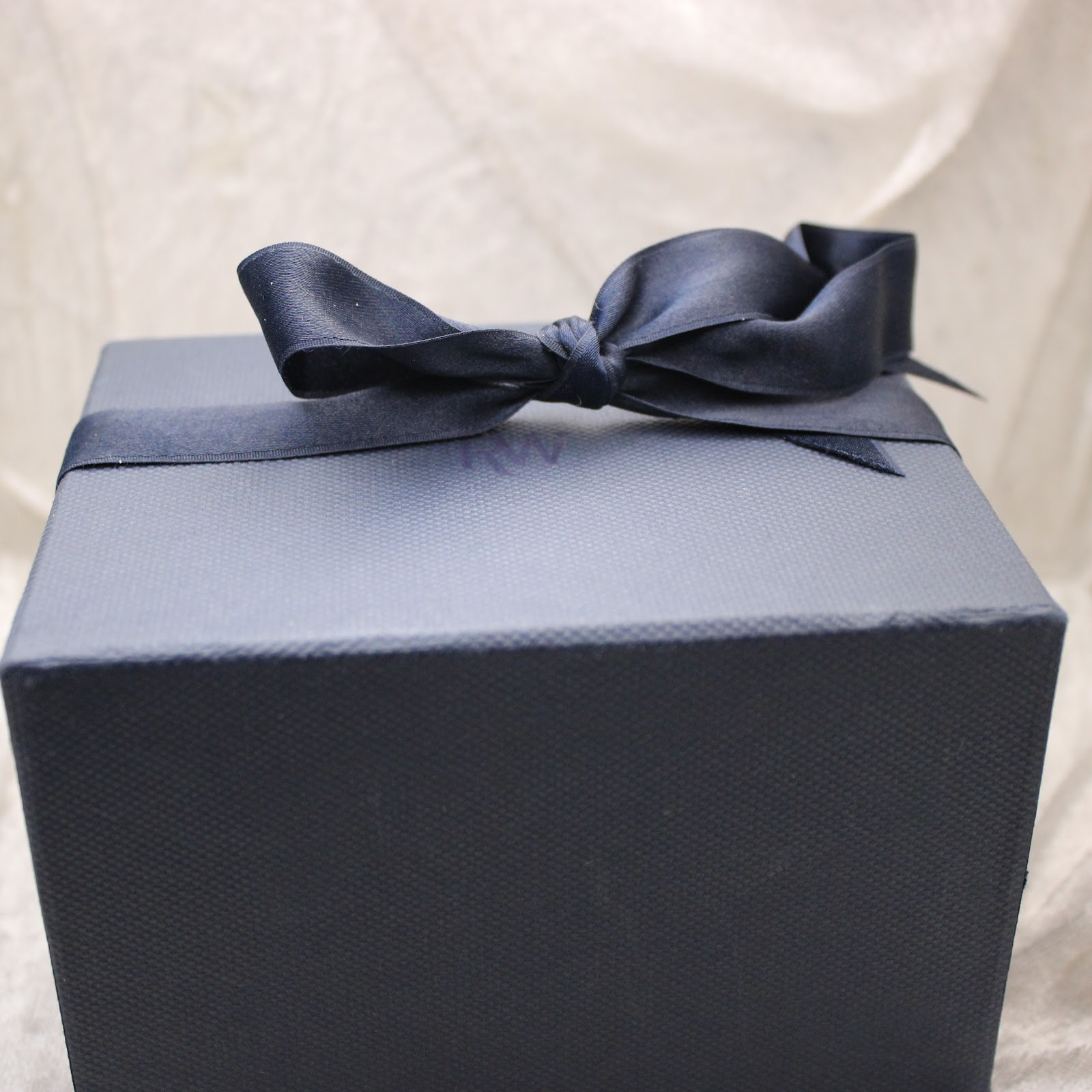 Close-up of the closed dark blue Raymond Weil watch box, tied with a matching blue ribbon.