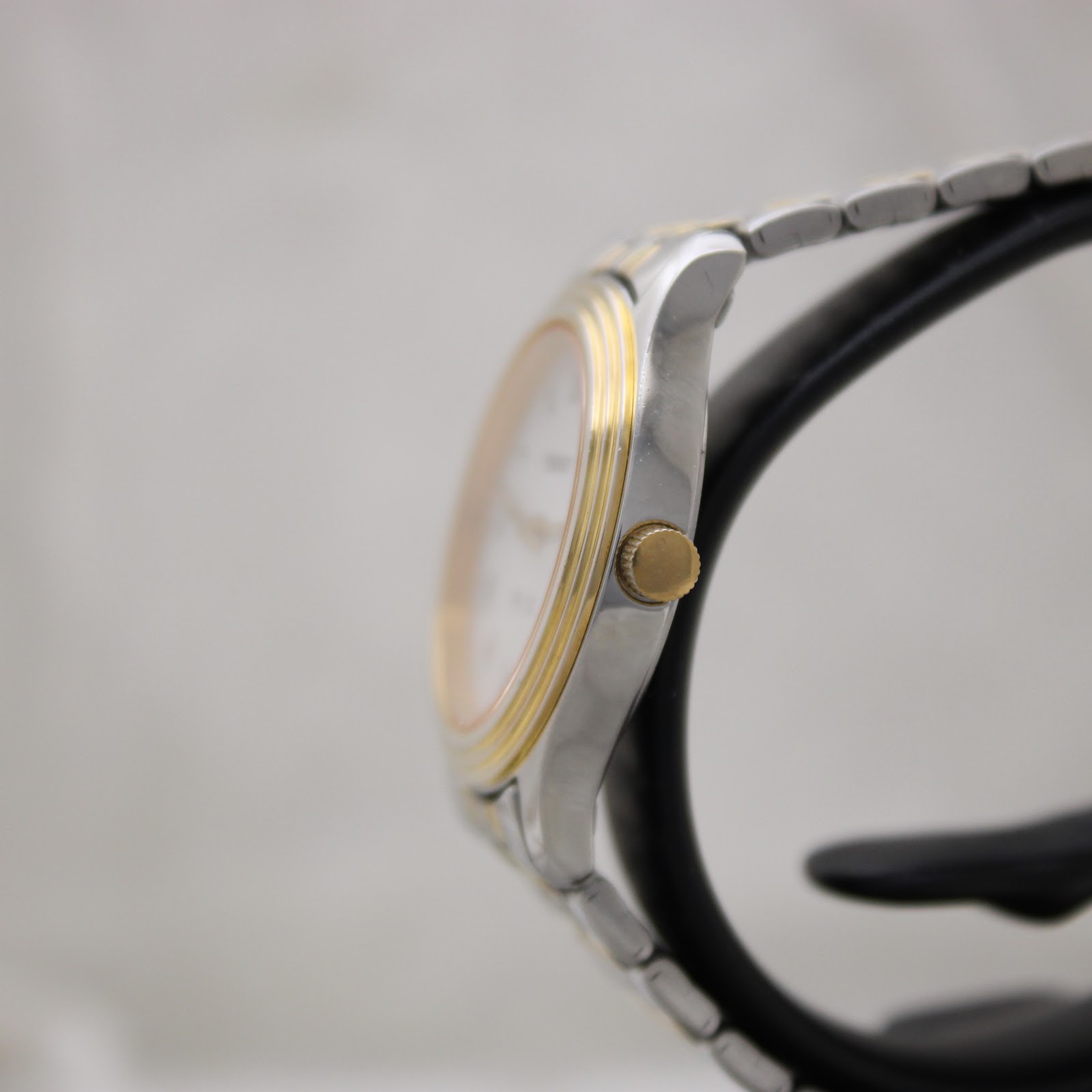 Side profile view of the Tissot PR 50, showing the gold-tone crown, bezel detail, and polished stainless steel case on a watch stand.