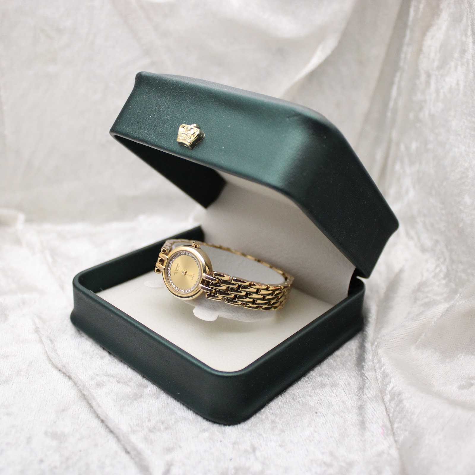 The Raymond Weil watch nestled inside a dark green presentation box with a gold crown emblem.