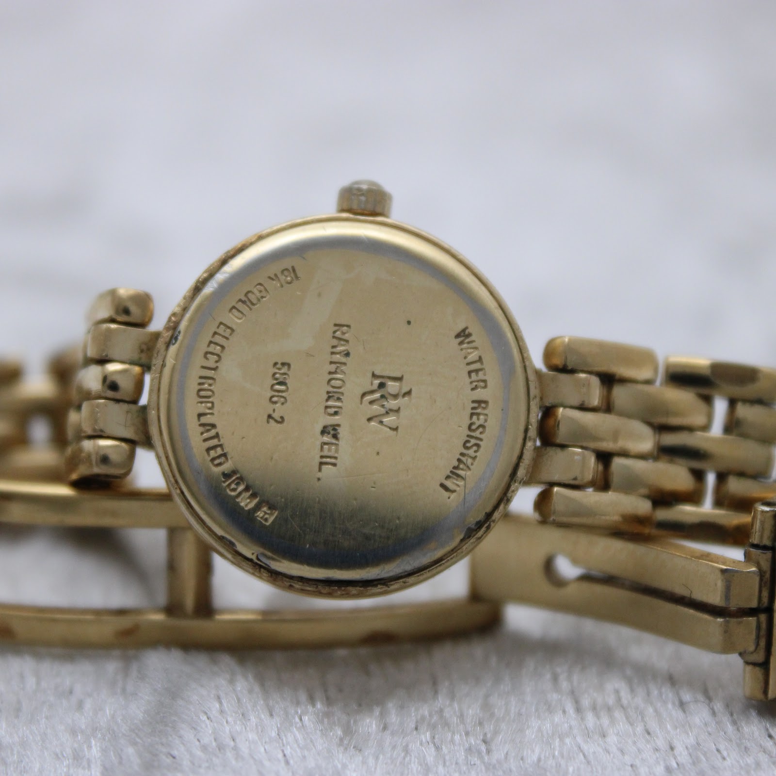Close-up of the gold-tone case back of the Raymond Weil watch, showing "18K GOLD ELECTROPLATED", "WATER RESISTANT", and model details.