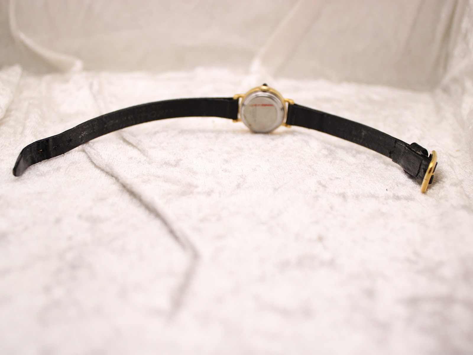 Full length view of the watch on its black leather strap, laid out on a white surface, showing the gold-tone buckle.