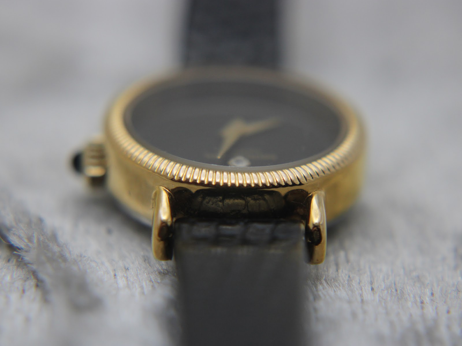 Side view close-up of the gold-plated watch case and lugs, with part of the black leather strap visible.